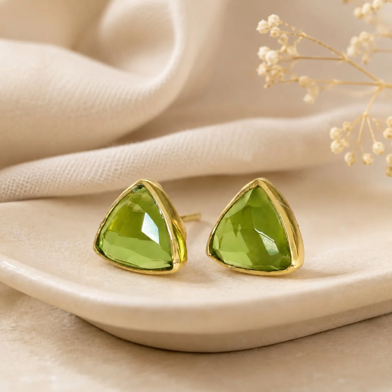 Peridot Edelstein Geburtsstein Ohrringe auf eleganter Keramik-Schmuckschale mit dekorativem Stoff arrangiert