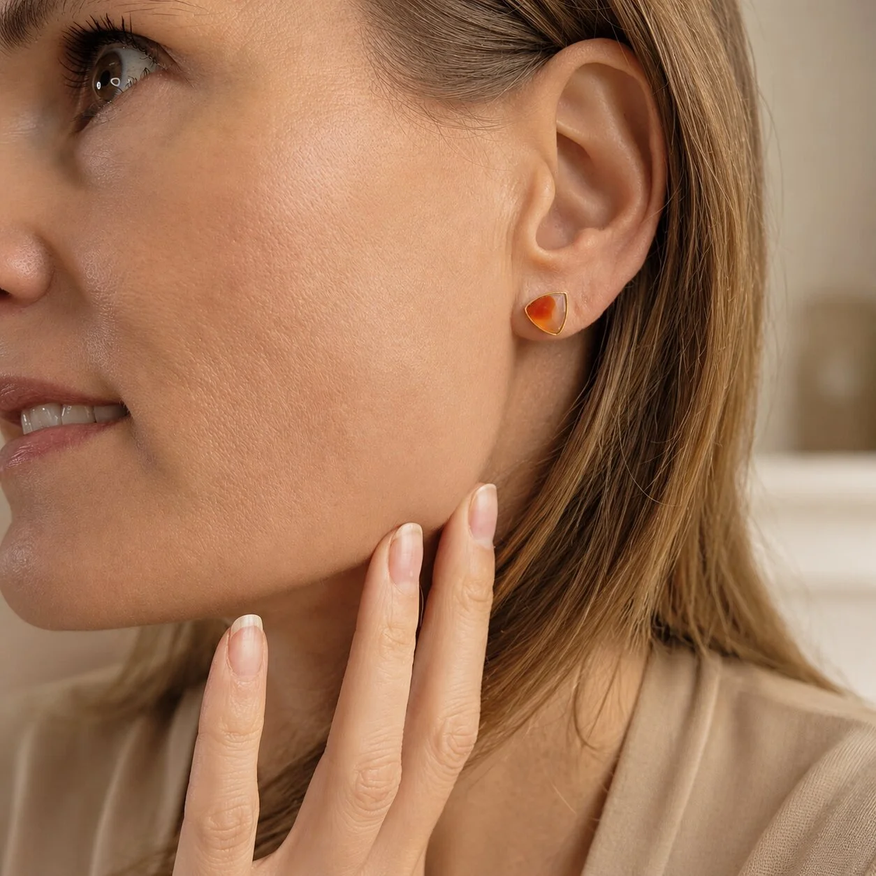 Nahaufnahme eines Models mit orangefarbenen Sardonyx Geburtsstein Ohrringen für August in vergoldeter Fassung