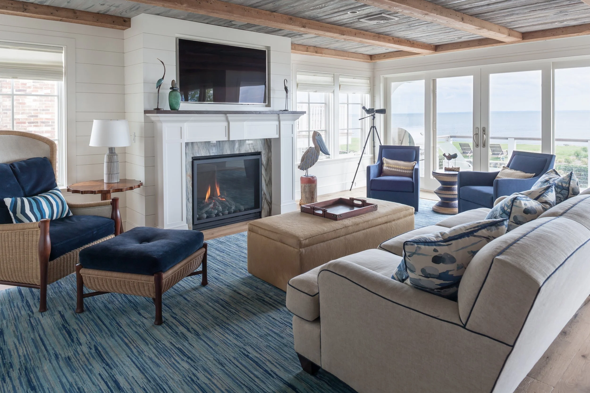 Coastal living room with sectional sofa, armchairs, fireplace, ocean view through large windows, telescope, and decorative items.