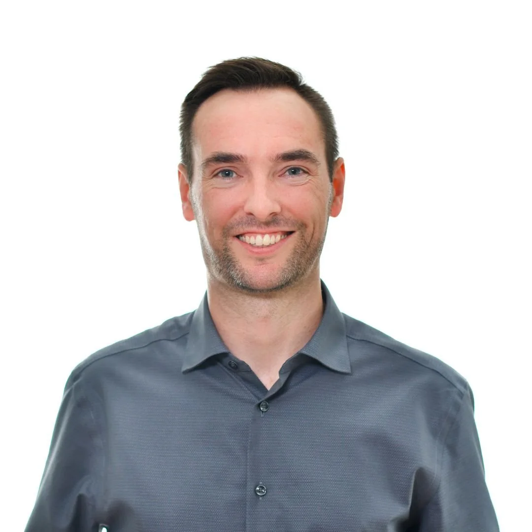Headshot of a smiling man with dark hair, wearing a dark gray shirt, against a plain white background.