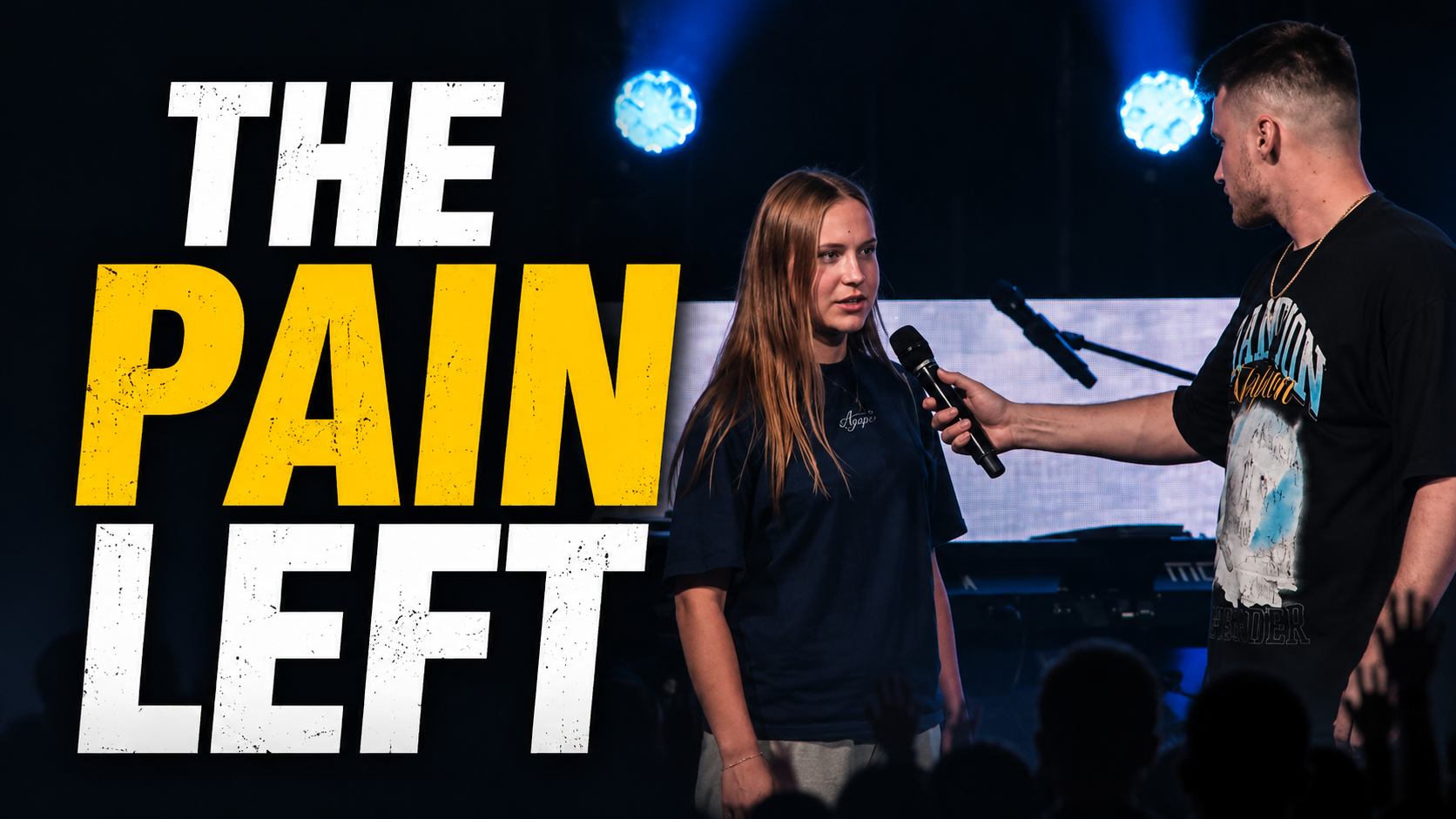 A young woman with long red hair speaking into a microphone on stage, being interviewed by a man holding the microphone, behind her, there is a large screen with the words 'The Pain Left' in big, bold letters. The stage has blue lights and a keyboard in the background.