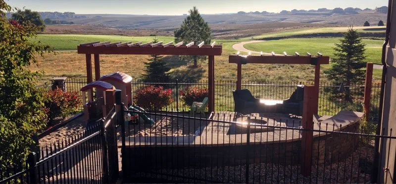 Backyard deck with pergolas, swing, and outdoor furniture overlooking open fields and hills in the distance.