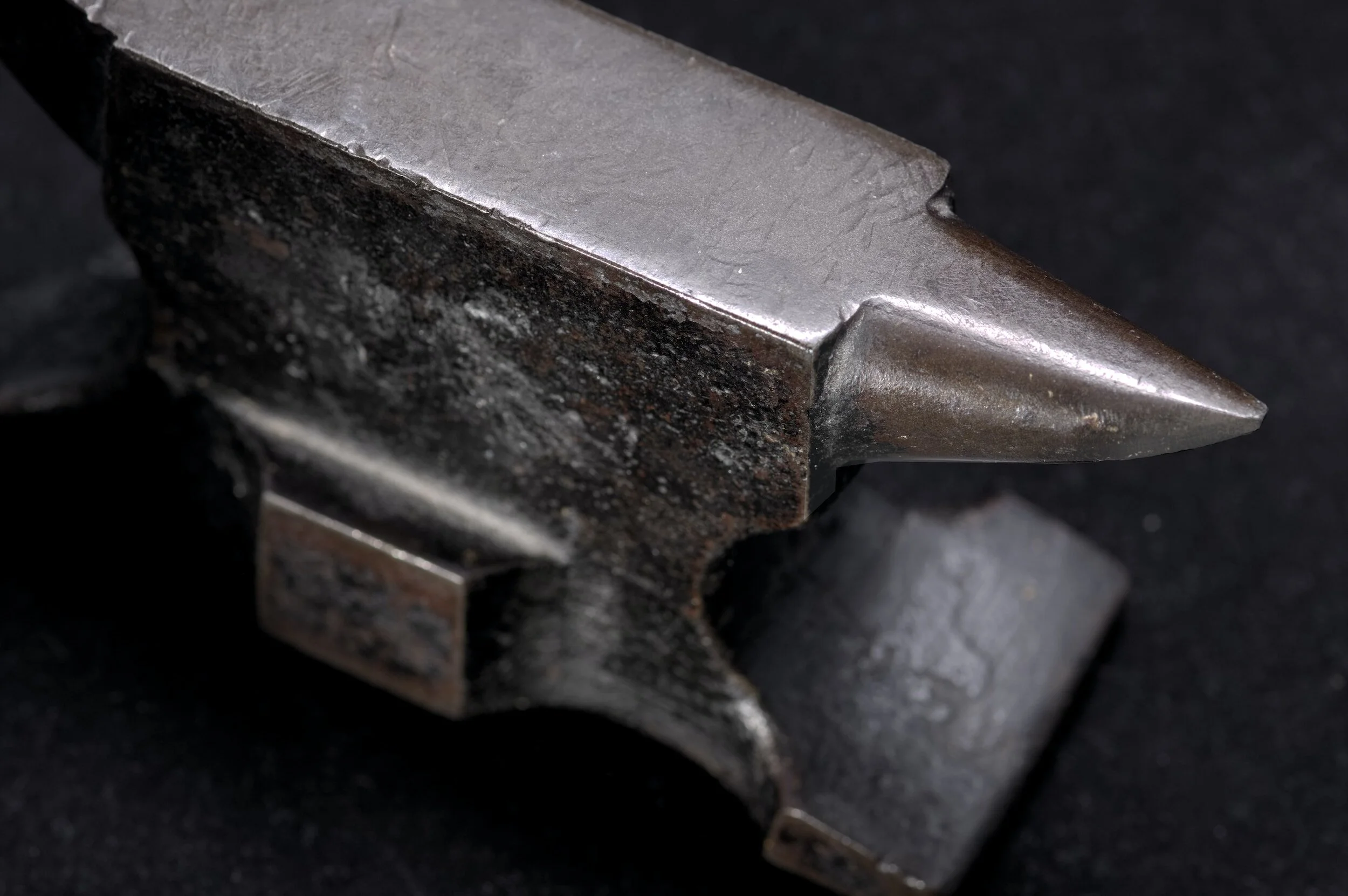 Close-up image of a metal chisel with a sharp pointed tip, showing signs of wear and tear, set against a dark background.