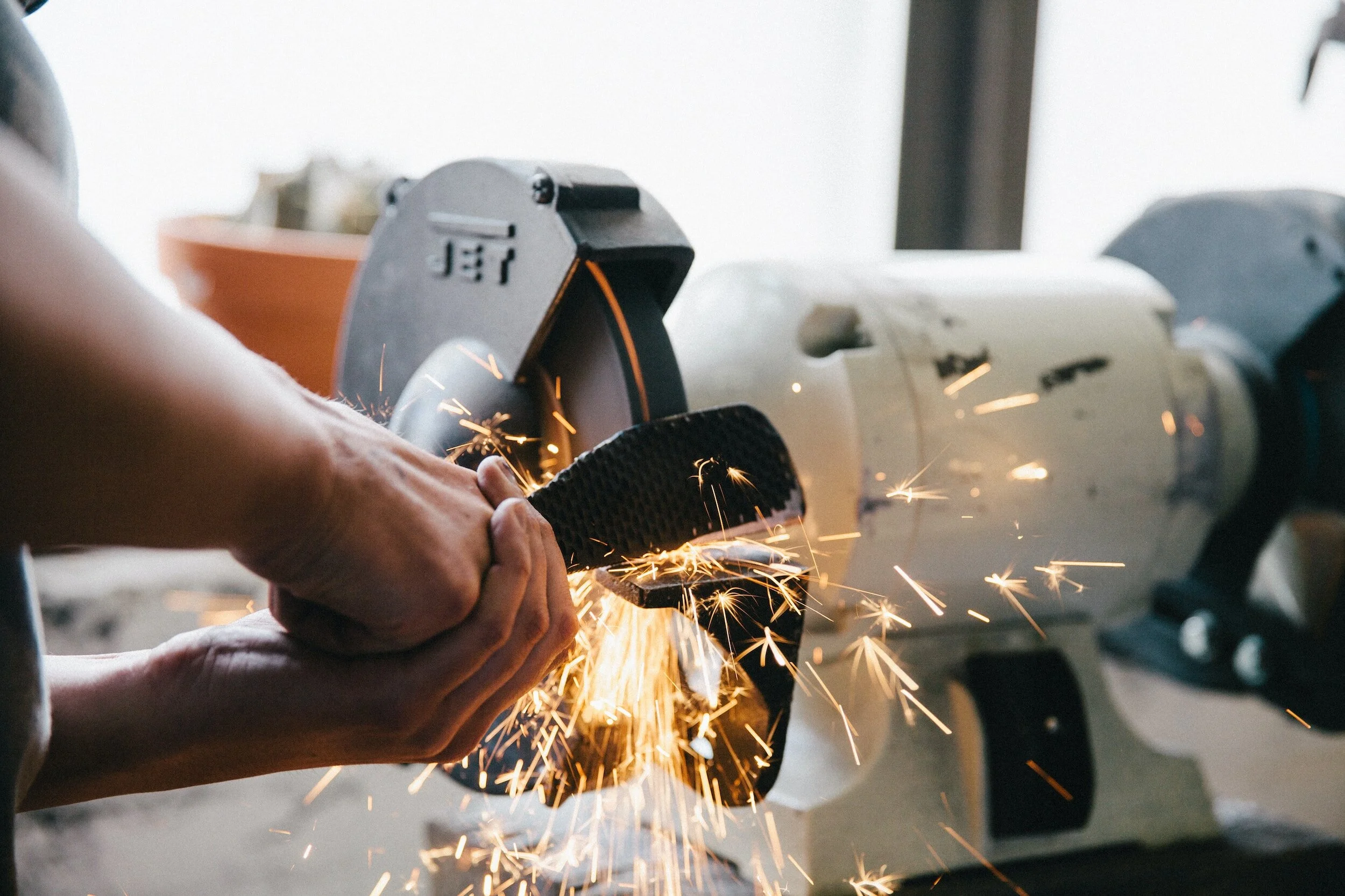 Person grinding metal with sparks flying, workshop setting with machinery.