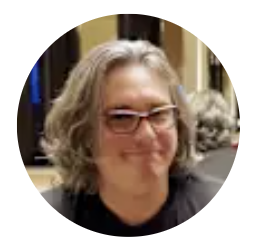 A woman with gray, curly hair and glasses smiling at the camera.