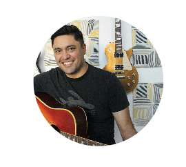 A man smiling and holding an acoustic guitar in a room with colorful geometric patterned wall art.