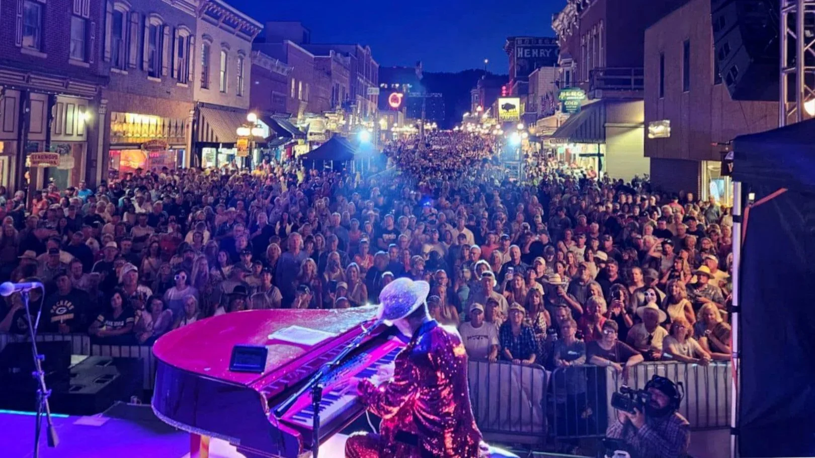 Elton Dan, an Elton John tribute artist, playing a red piano on stage in front of thousands of people at a street party.