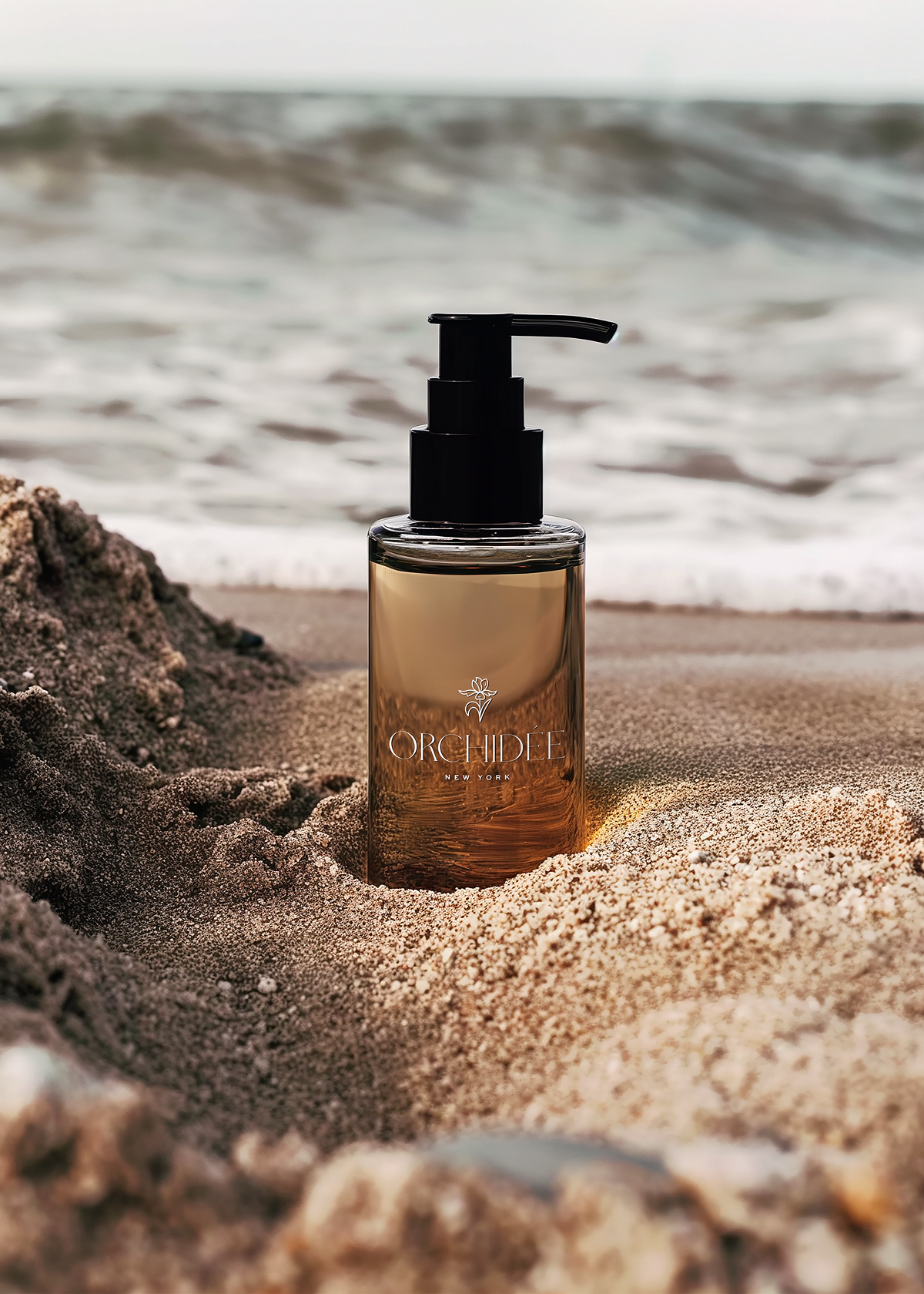 A perfume bottle labeled 'Orchidée New York' on sandy beach with ocean waves in background.
