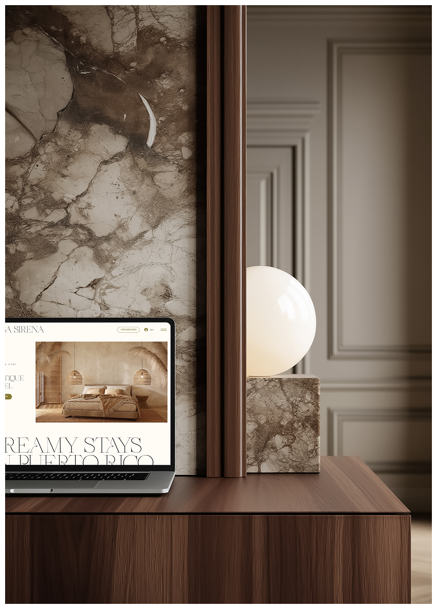 Close-up of a wooden cabinet with a marble wall behind it, a computer screen displaying a bedroom interior, and a white spherical lamp on a marble base, in a sophisticated interior setting.