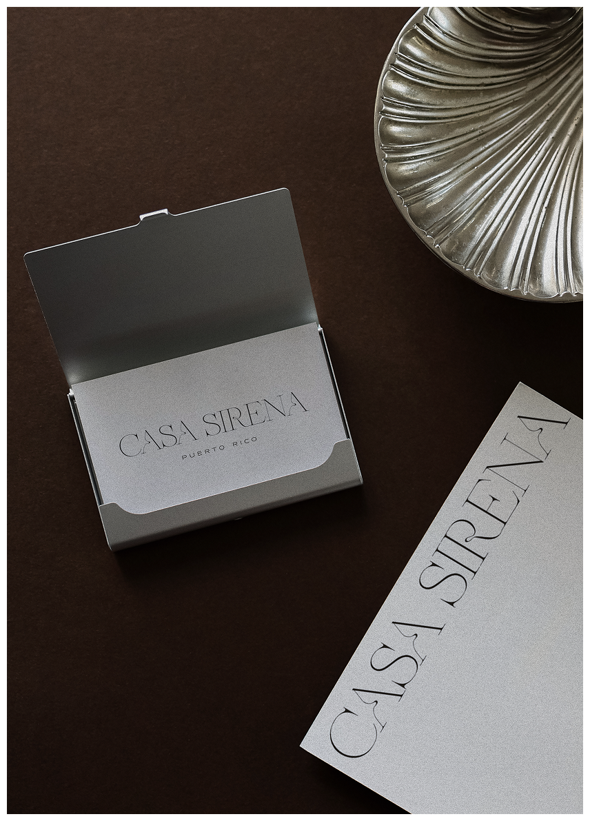 A silver jewelry box labeled 'CASA SIRENA PUERTO RICO' on a dark surface, with a decorative metal bowl and a printed sheet of paper nearby.