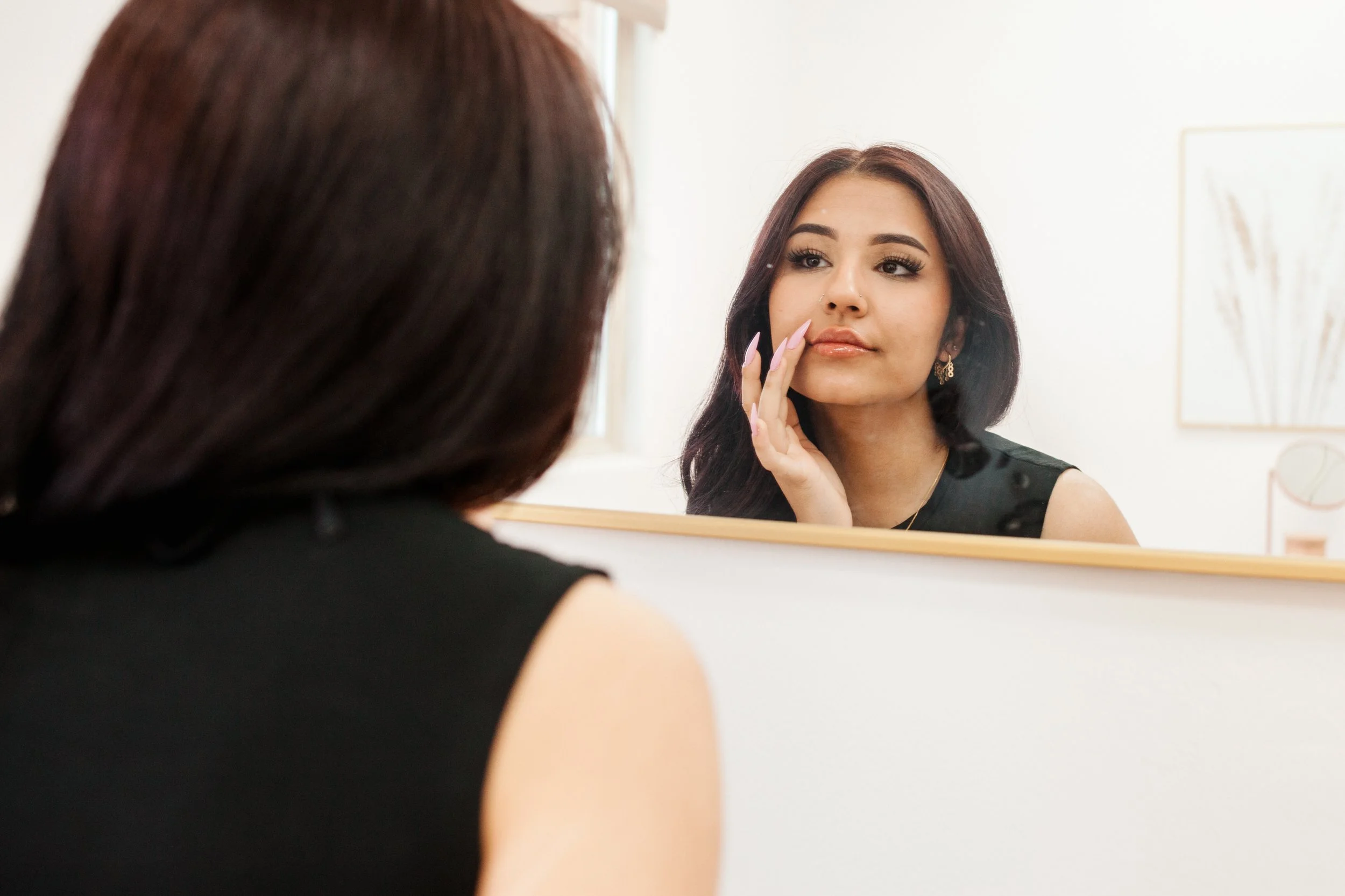 Woman looking at herself in a mirror, touching her face with her hand.