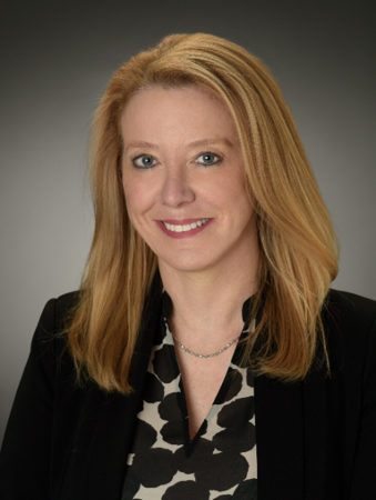Professional woman with blonde hair smiling, wearing a black blazer and patterned blouse