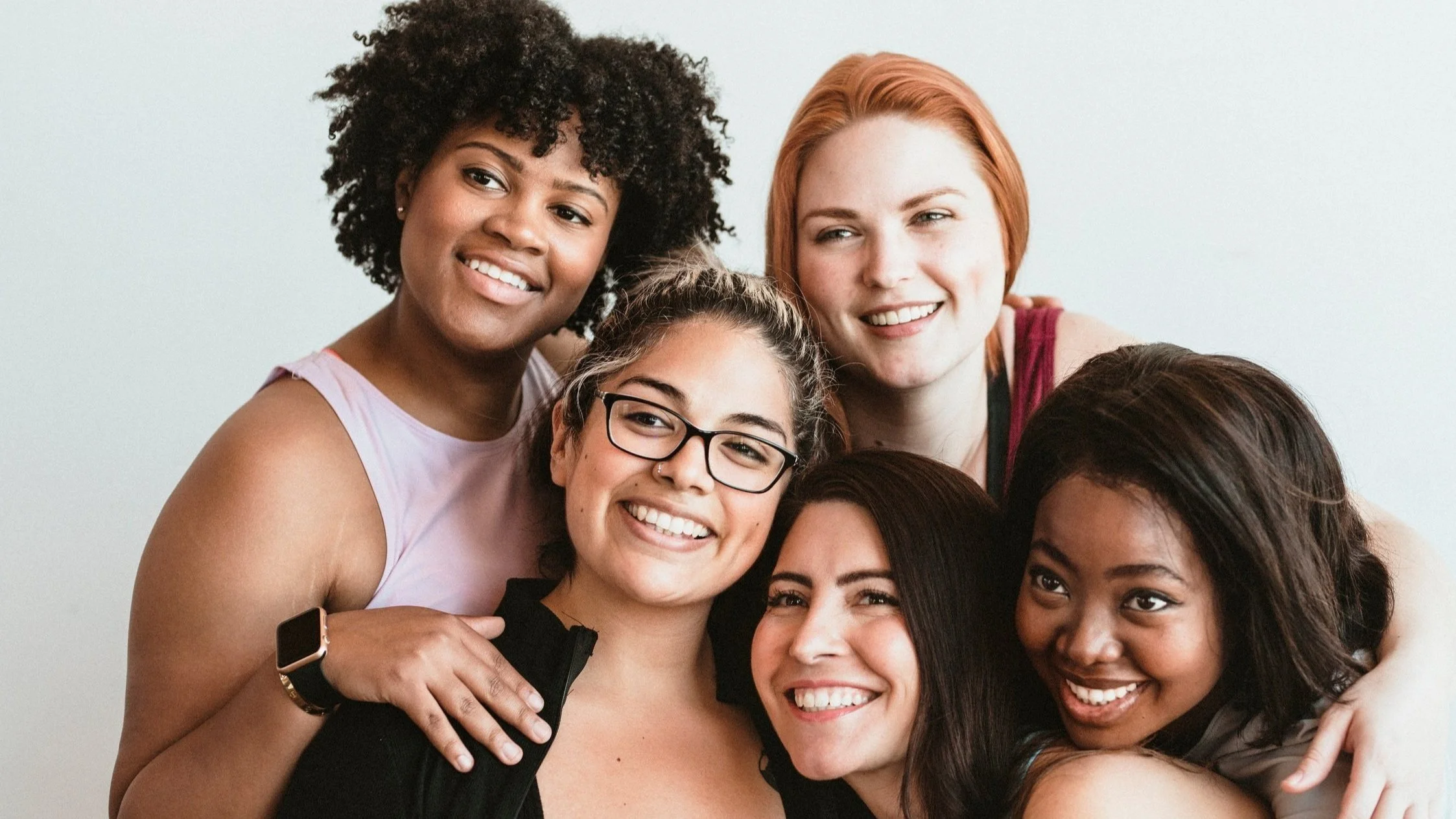 Group of six women smiling and hugging each other.