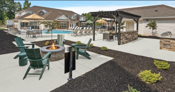 Community outdoor pool area with fire pit, seating, and a pergola, surrounded by houses and landscaping.