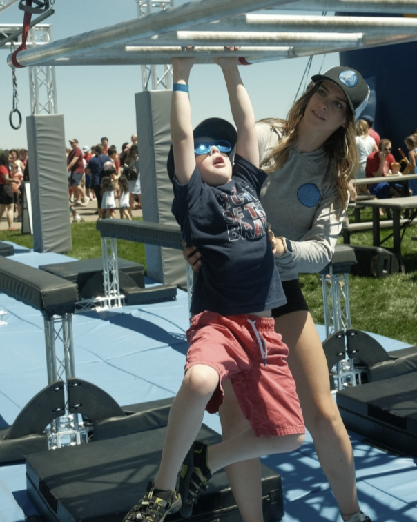 Ark Ninja coach Jae Bennett spotting a young boy on the outdoor mobile ninja warrior course.