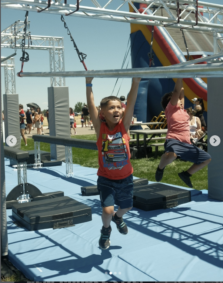 Kids navigating upper-body obstacles on the Ark Ninja mobile course at an outdoor community event.