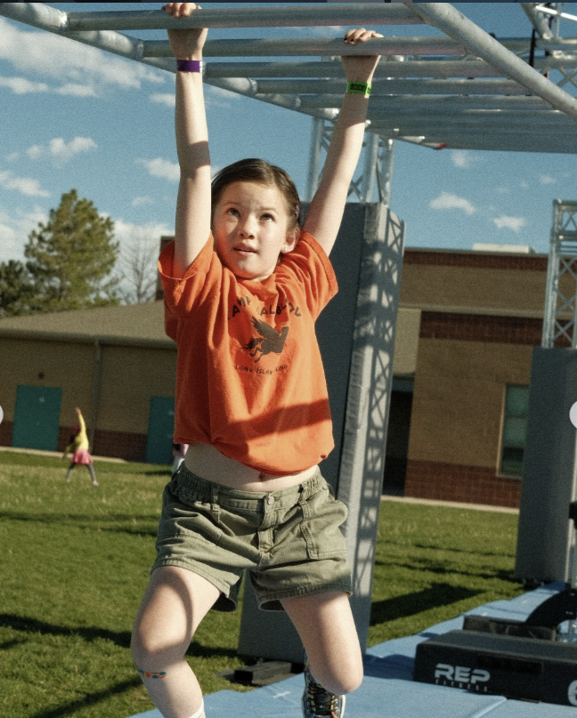Young girl conquering the monkey bars on the Ark Ninja outdoor mobile course.
