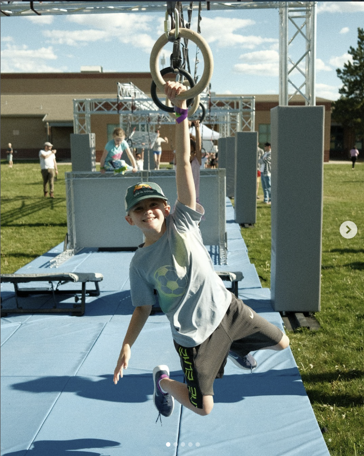 Young participant enjoying ring obstacles on Ark Ninja's portable course during a outdoor event.