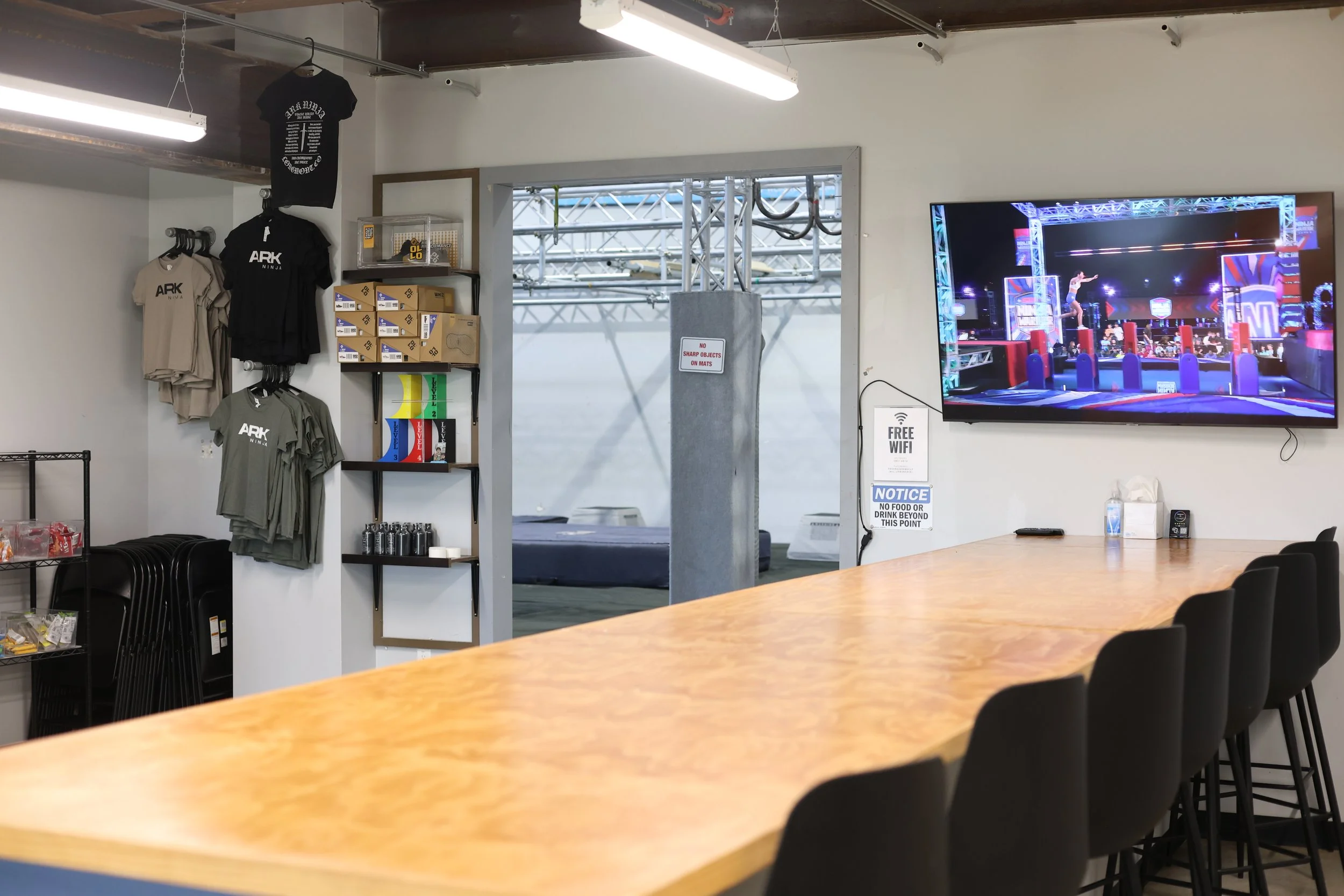 Ark Ninja lobby with America Ninja Warrior on the Screen and branded Ark Ninja T-shirts.