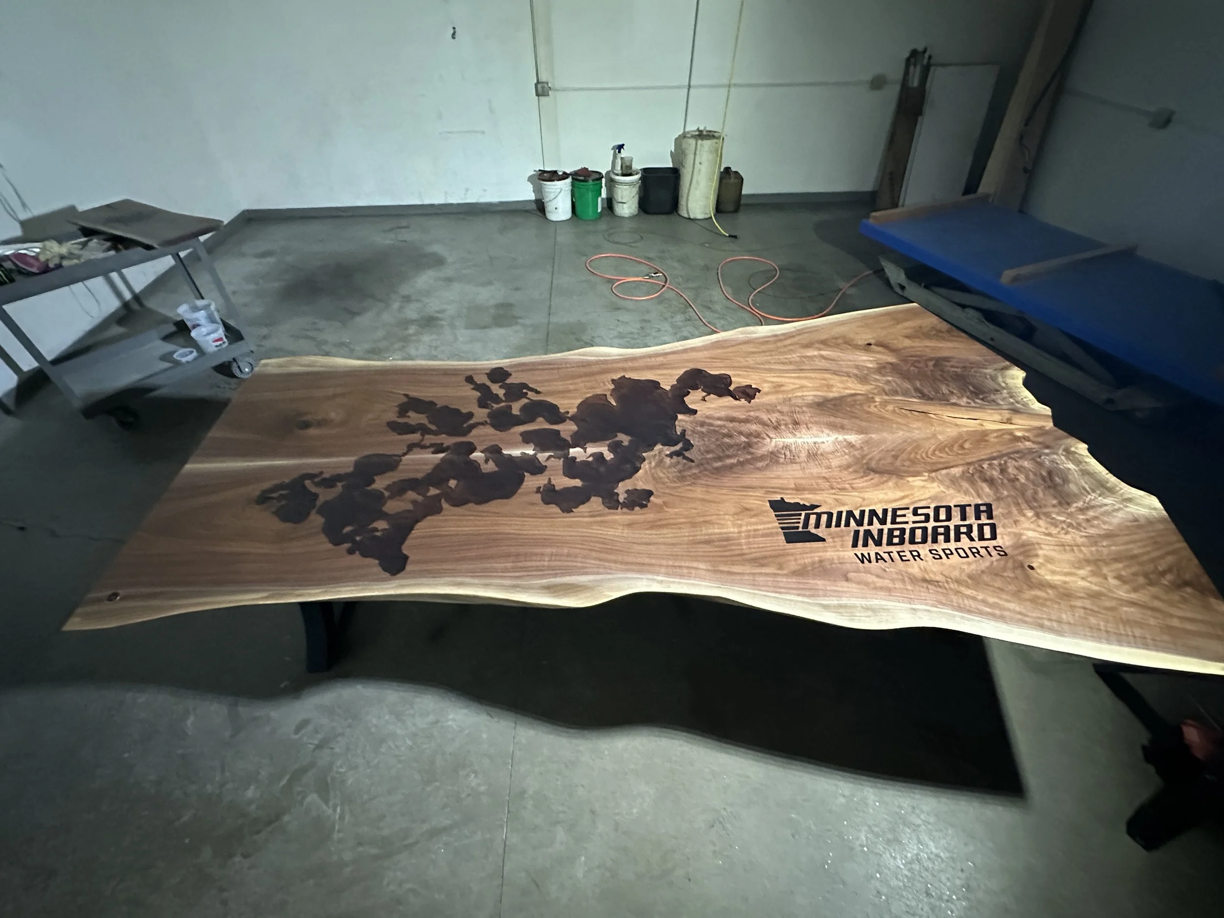 A wooden paddle with the logo 'Minnesota Inboard Water Sports' printed on it, resting on a concrete floor with various tools and cans in the background.