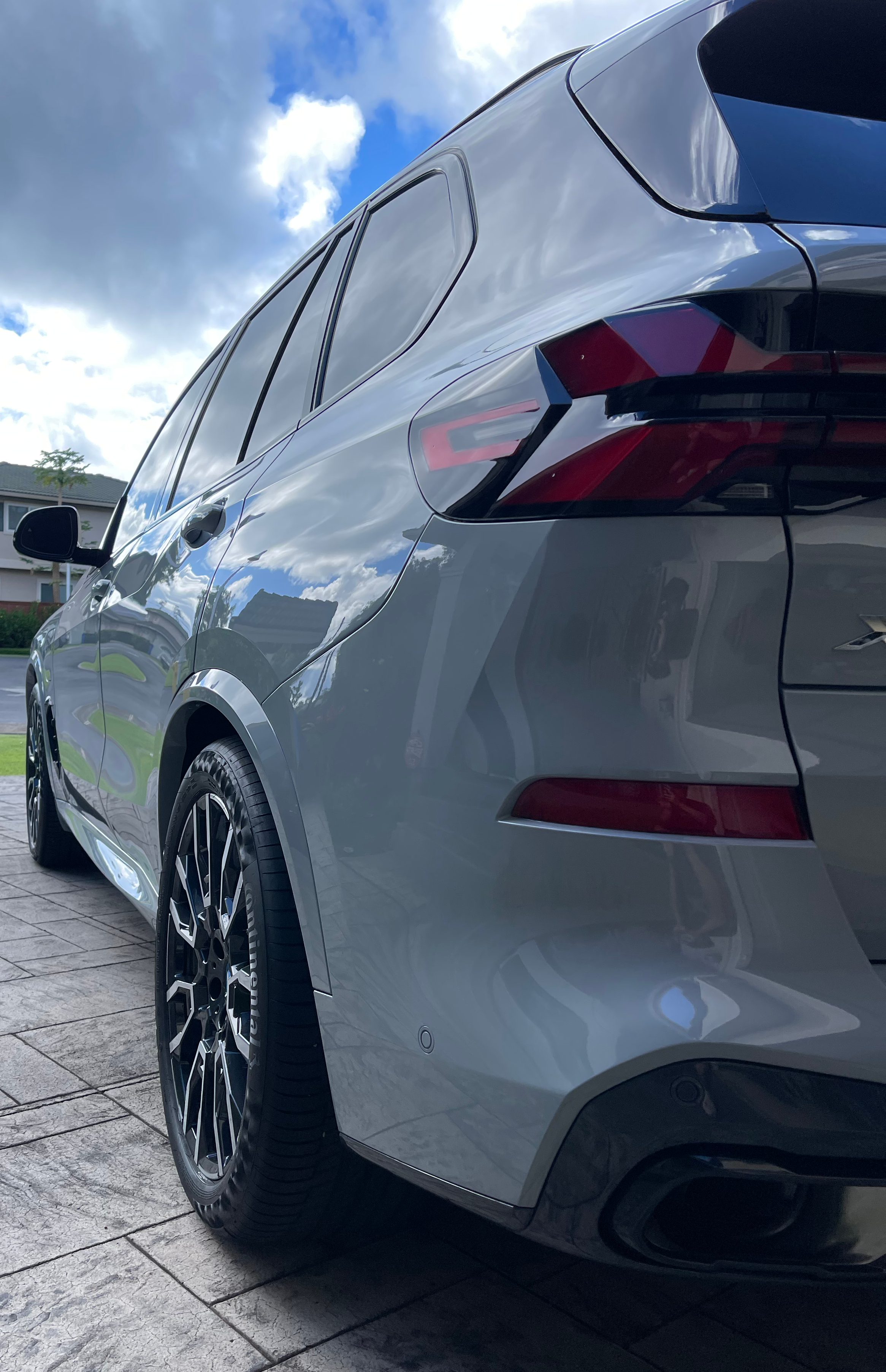 Low-angle view of a gray SUV with black alloy wheels and modern taillights, parked on a paved surface under a cloudy sky.