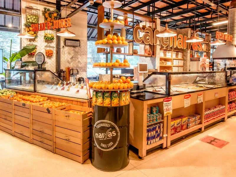 Fresh oranges displayed in wooden crates and on a round stand inside a grocery store, with shelves of other products and signs indicating produce and store branding.
