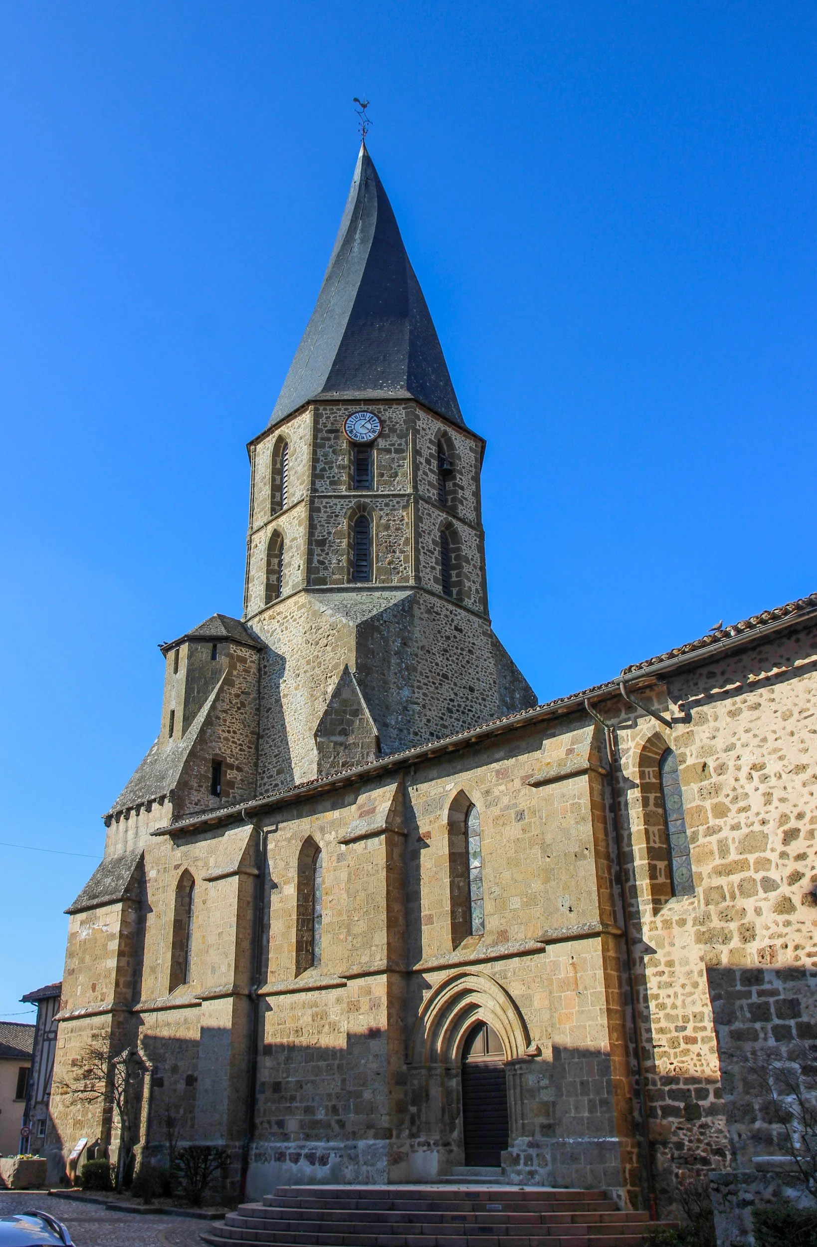 A stone church with a tall, pointed spire set against a clear blue sky.
