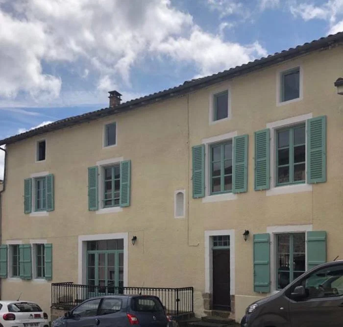 A yellow multi-story residential building with green shutters, black door, and parked cars in front.
