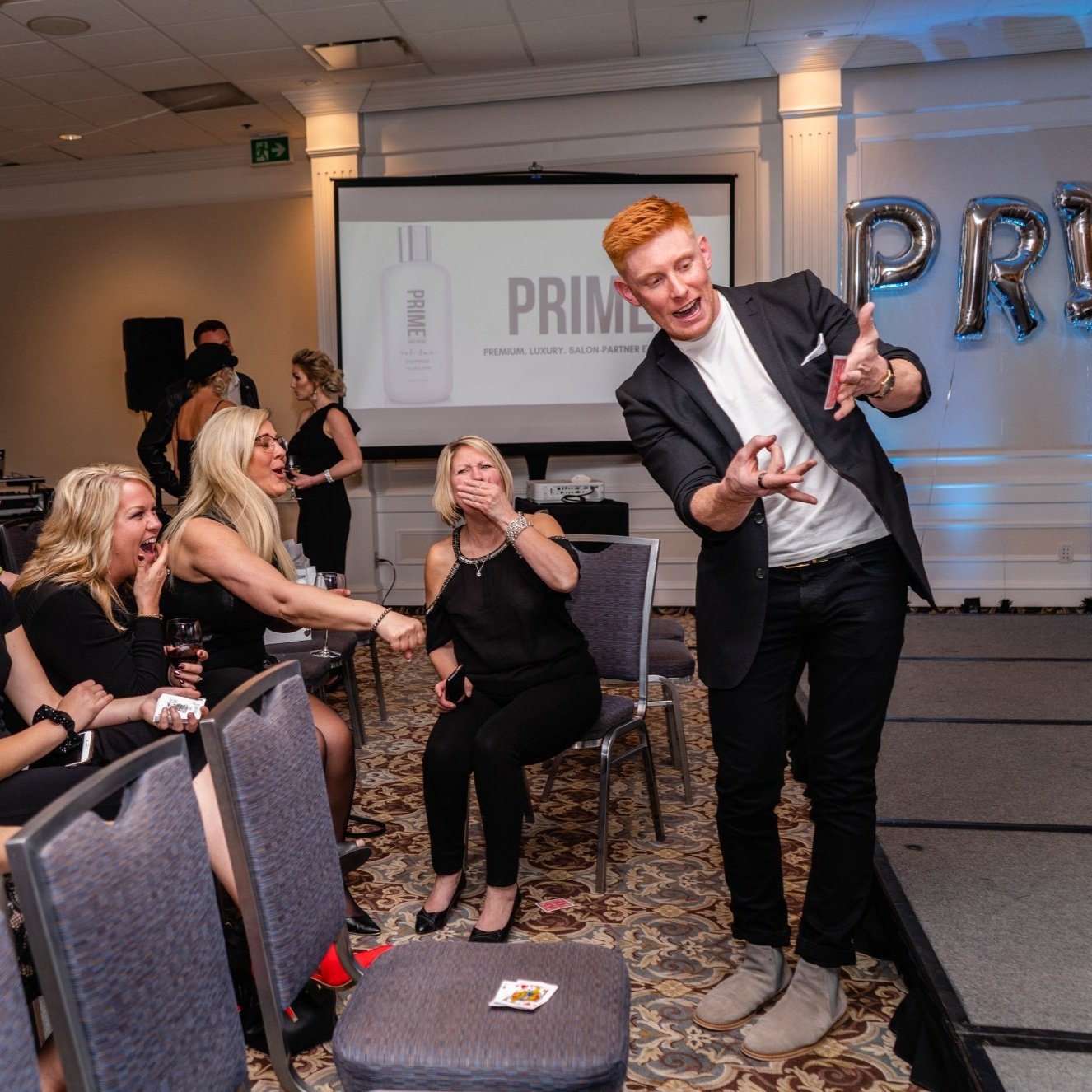  Matt Gore, a magician, captivates the audience as he stands in front of them, holding a card, presenting a magic trick 