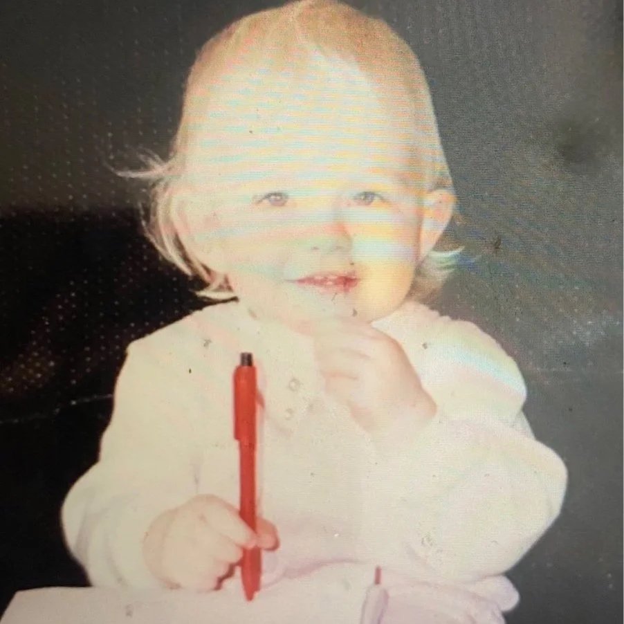 Picture of Erin as a toddler. She is holding a pen and notebook.