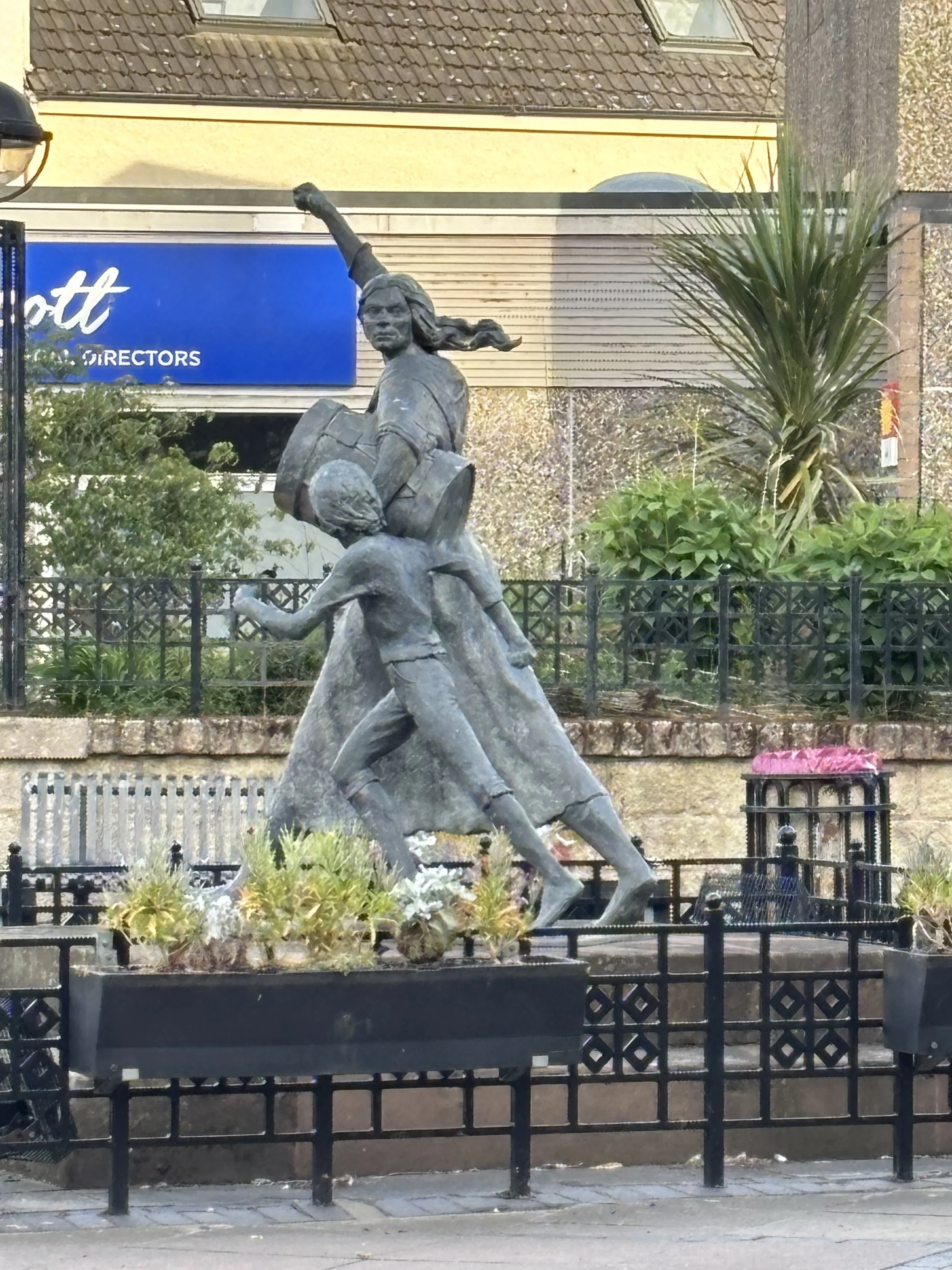 Statue dedicated to Jackie Crookston. Image shows a woman striding forward with a drum under her left arm and a boy running along beside her. Her right arm punches the air defiantly.