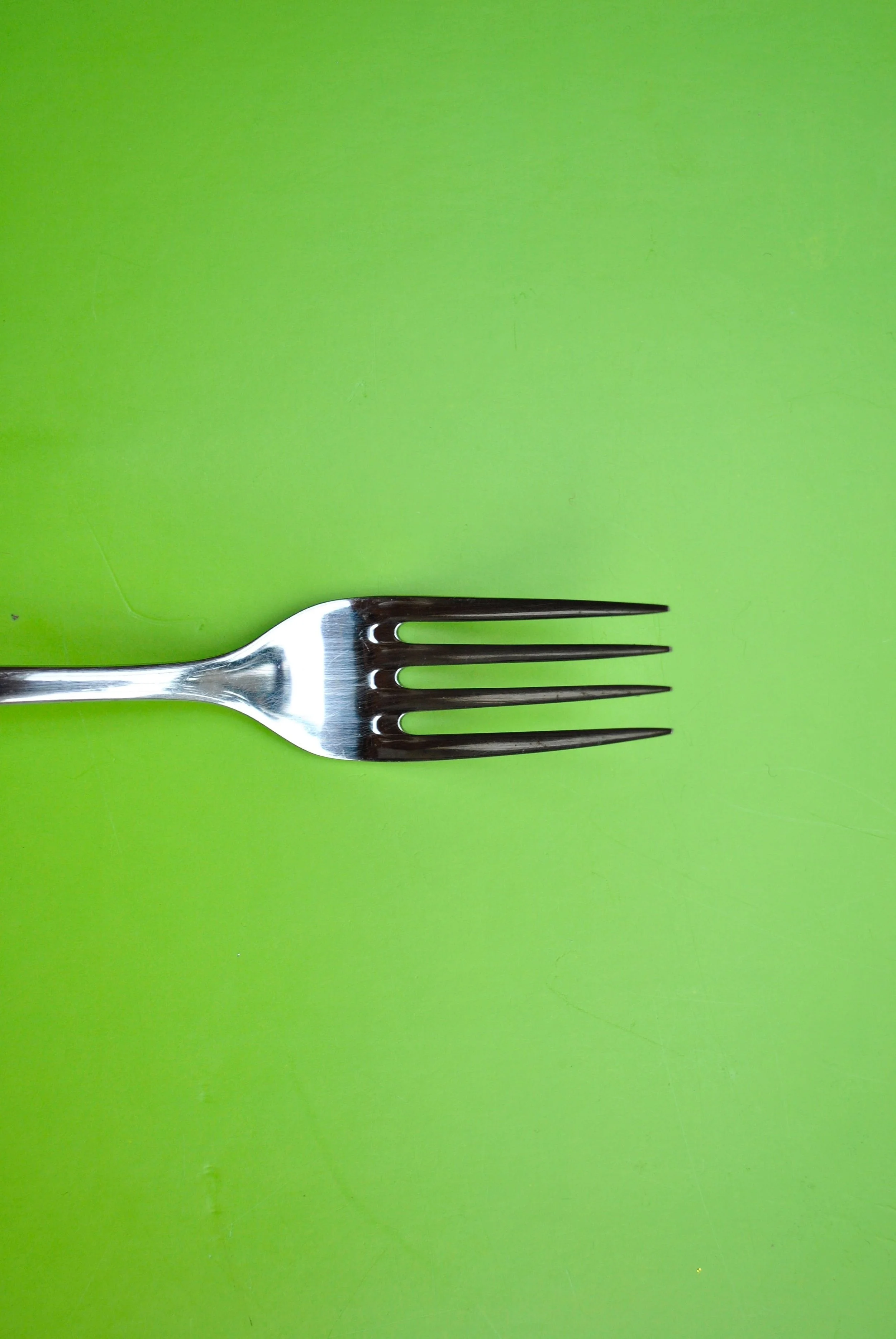 Silver fork with four tines on a bright green surface.