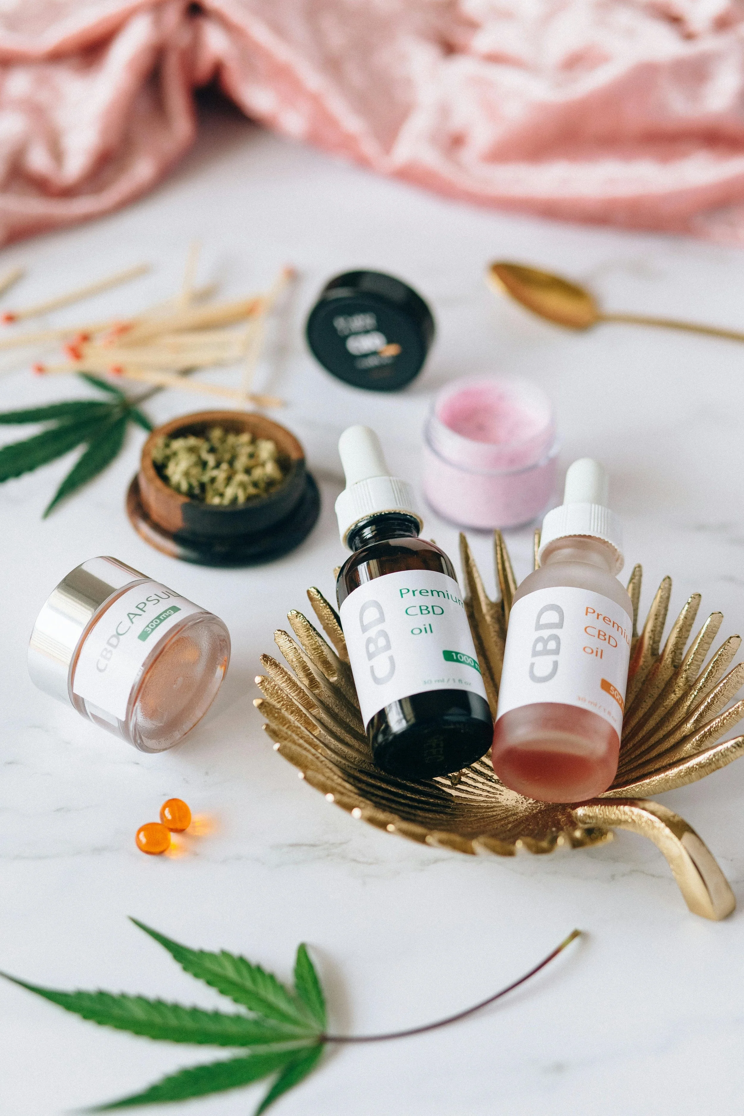 Assorted CBD products including oils, capsules, and topical creams arranged on a white surface with green cannabis leaves and wooden matches.