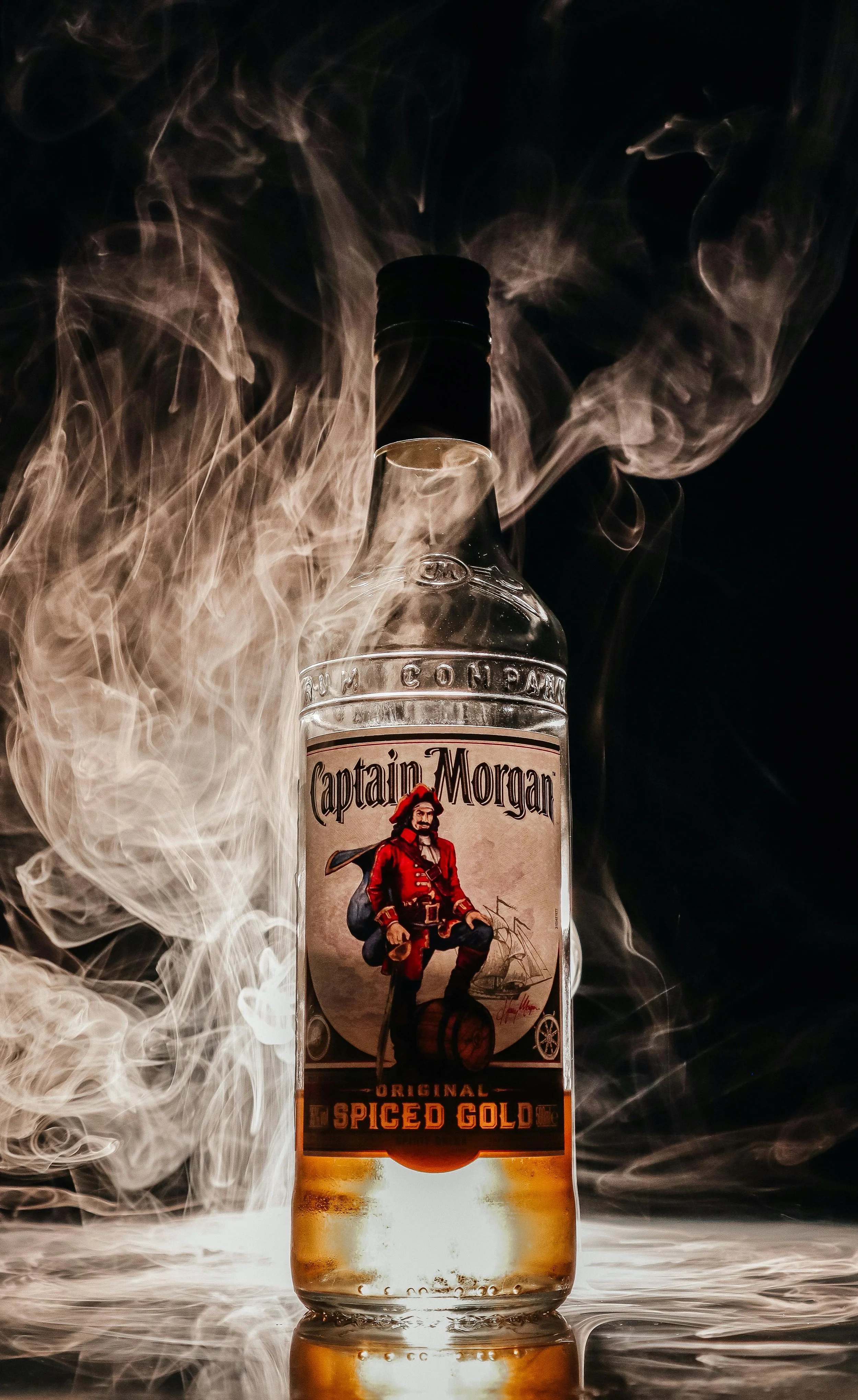 A bottle of Captain Morgan Spiced Gold rum surrounded by swirling smoke or vapor against a dark background.