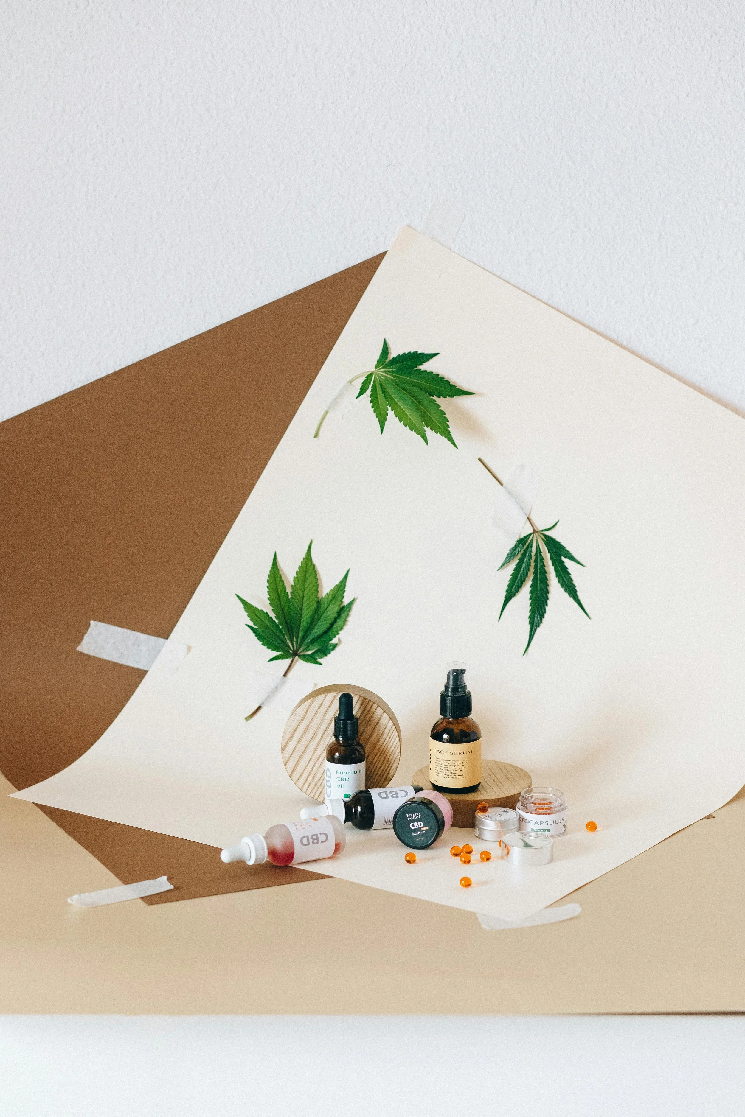 Collection of CBD products including bottles, capsules, and drops arranged with cannabis leaves on background paper.