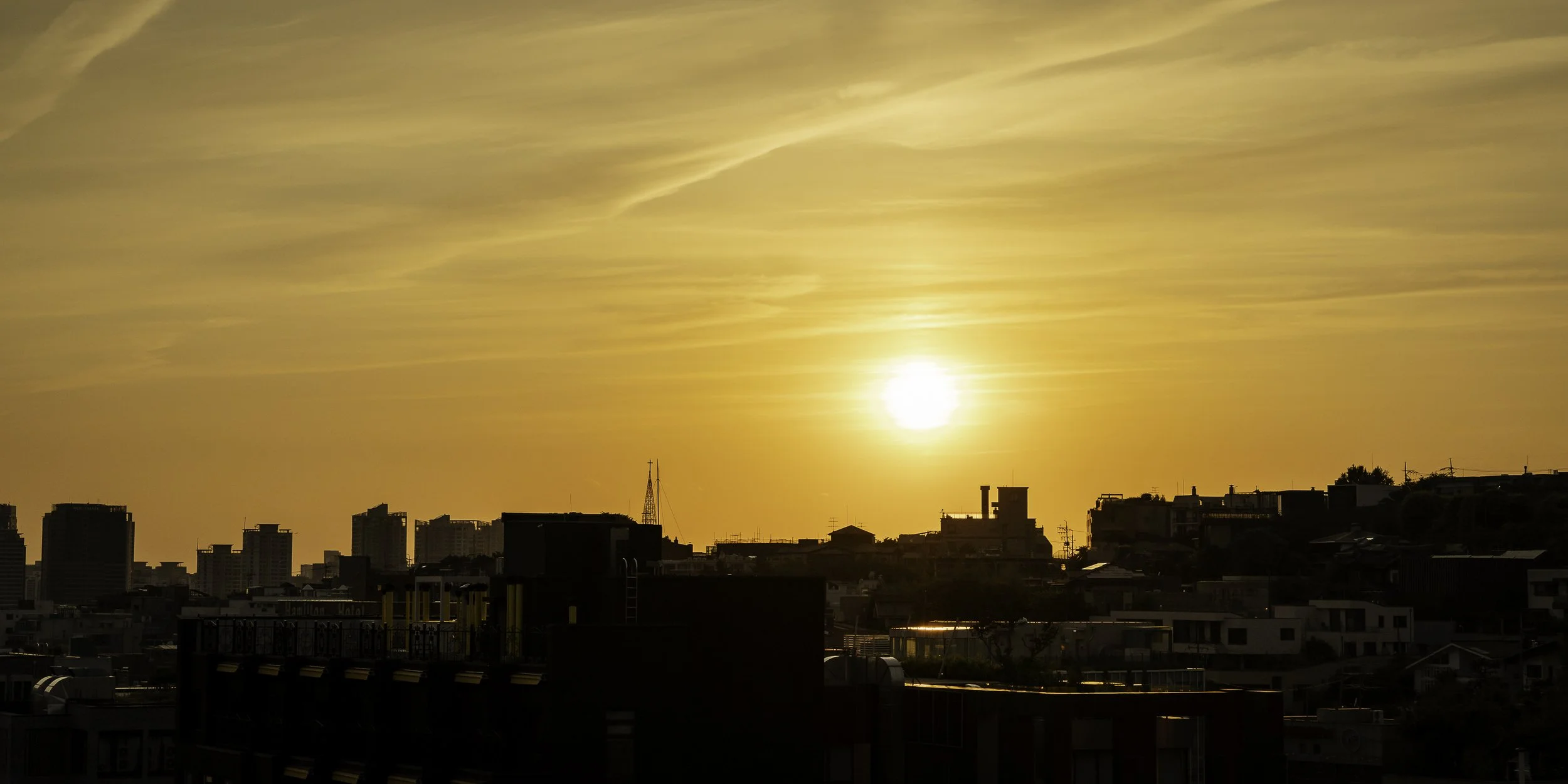 Sunset over a city skyline with high-rise buildings and residential homes, orange sky with clouds.