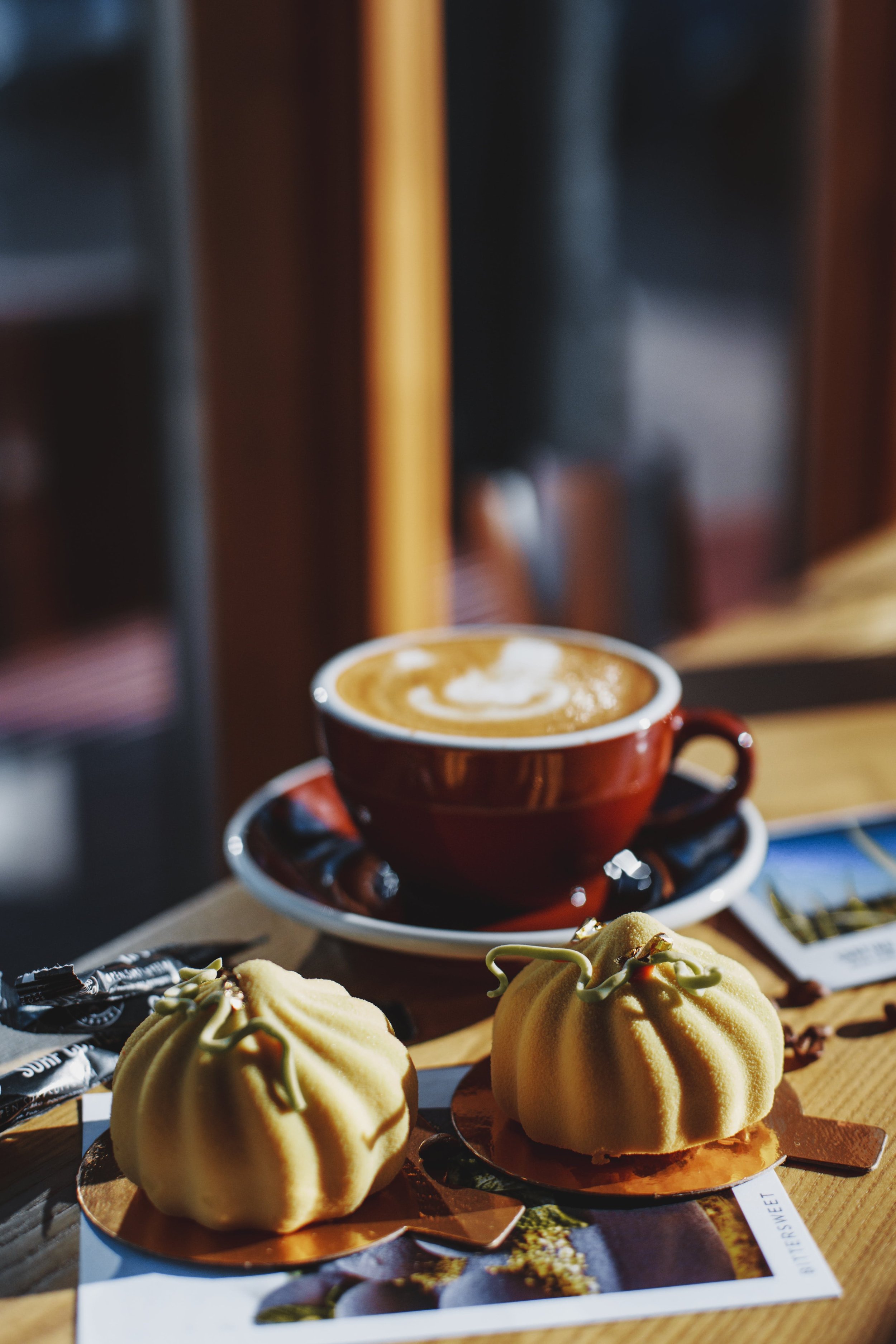 A cup of coffee with latte art and two decorative pumpkin-shaped desserts on a wooden table.