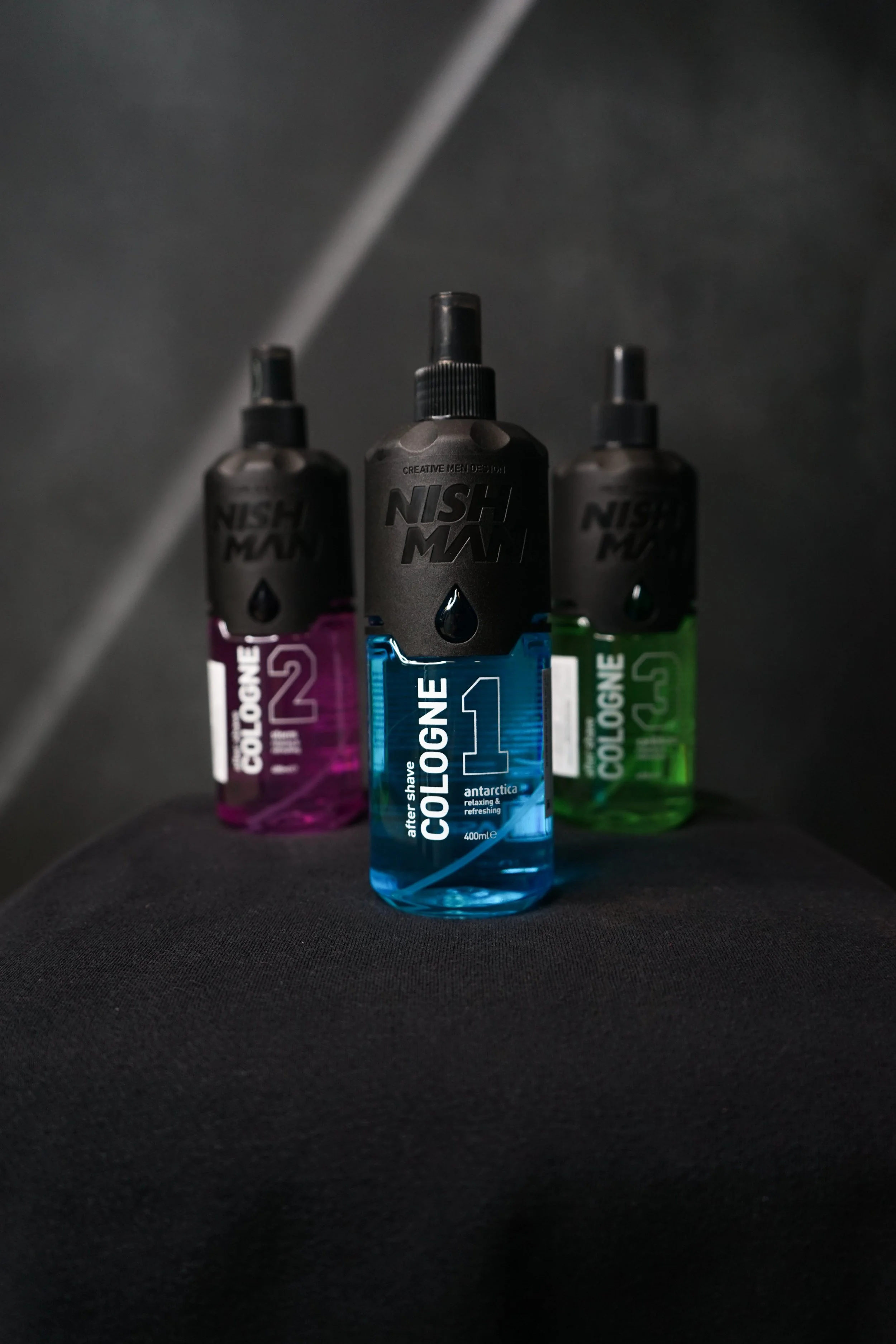 Three bottles of aftershave labeled 'Cologne 1' in blue, 'Cologne 2' in pink, and 'Cologne 3' in green, placed on a black surface.