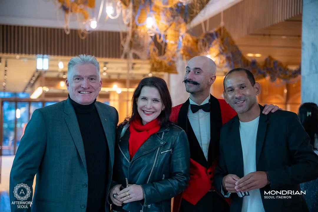 Four people posing together at a social event in Seoul, with festive lighting and decorations in the background.