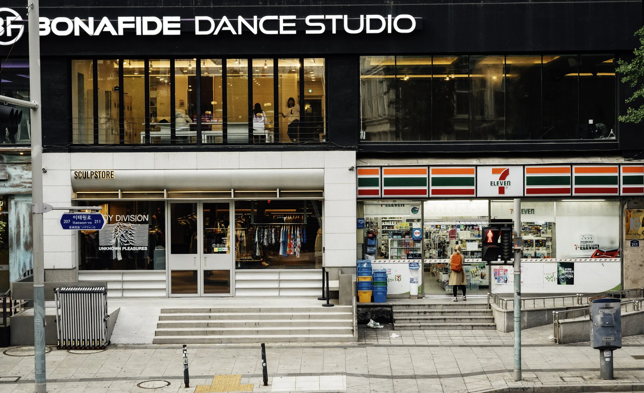 City street view with a Bonafide Dance Studio on the second floor and a 7-Eleven convenience store on the ground level, including a pedestrian crossing signal showing a red walking figure.
