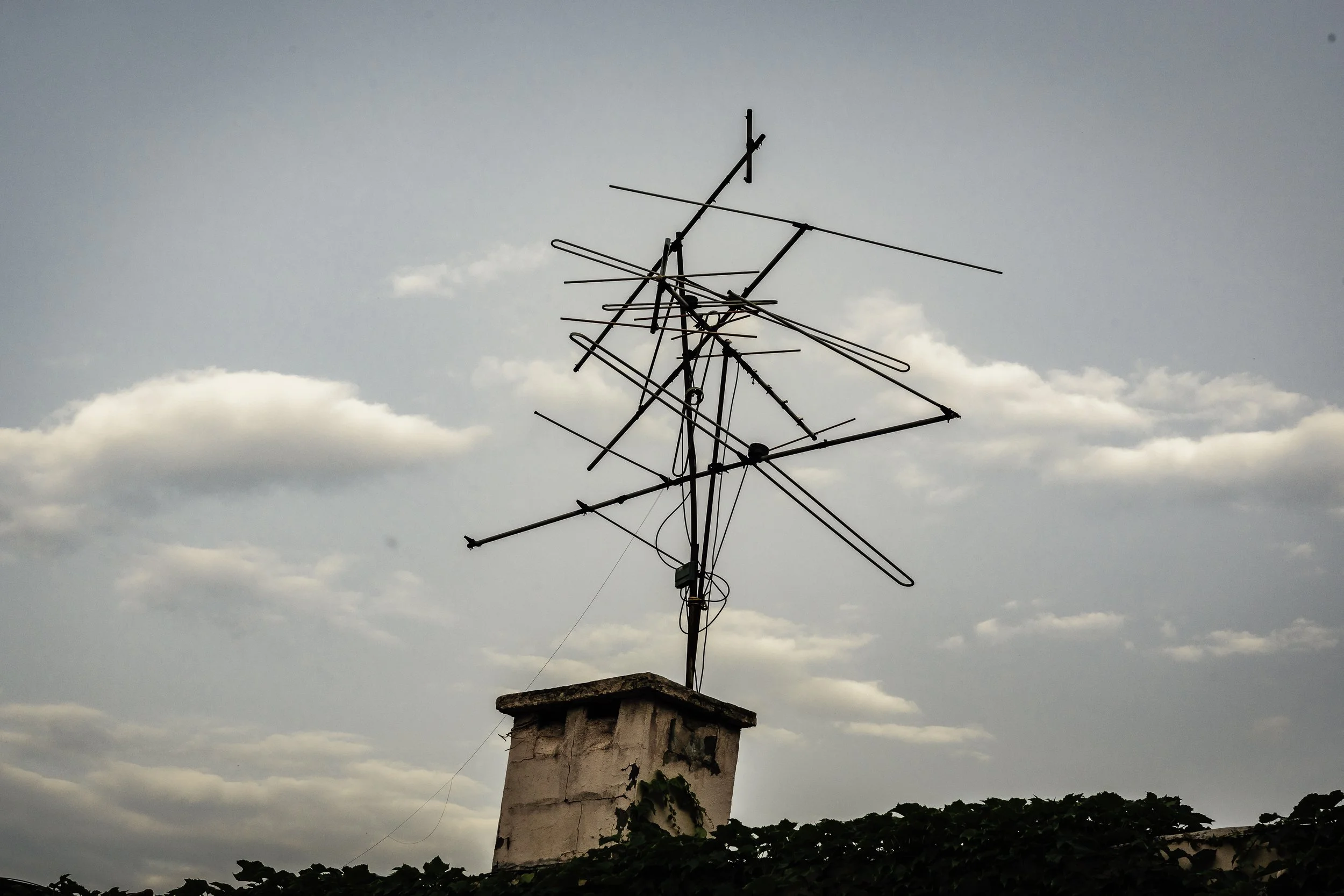 Television antennas atop a chimney on a rooftop, with a cloudy sky in the background.