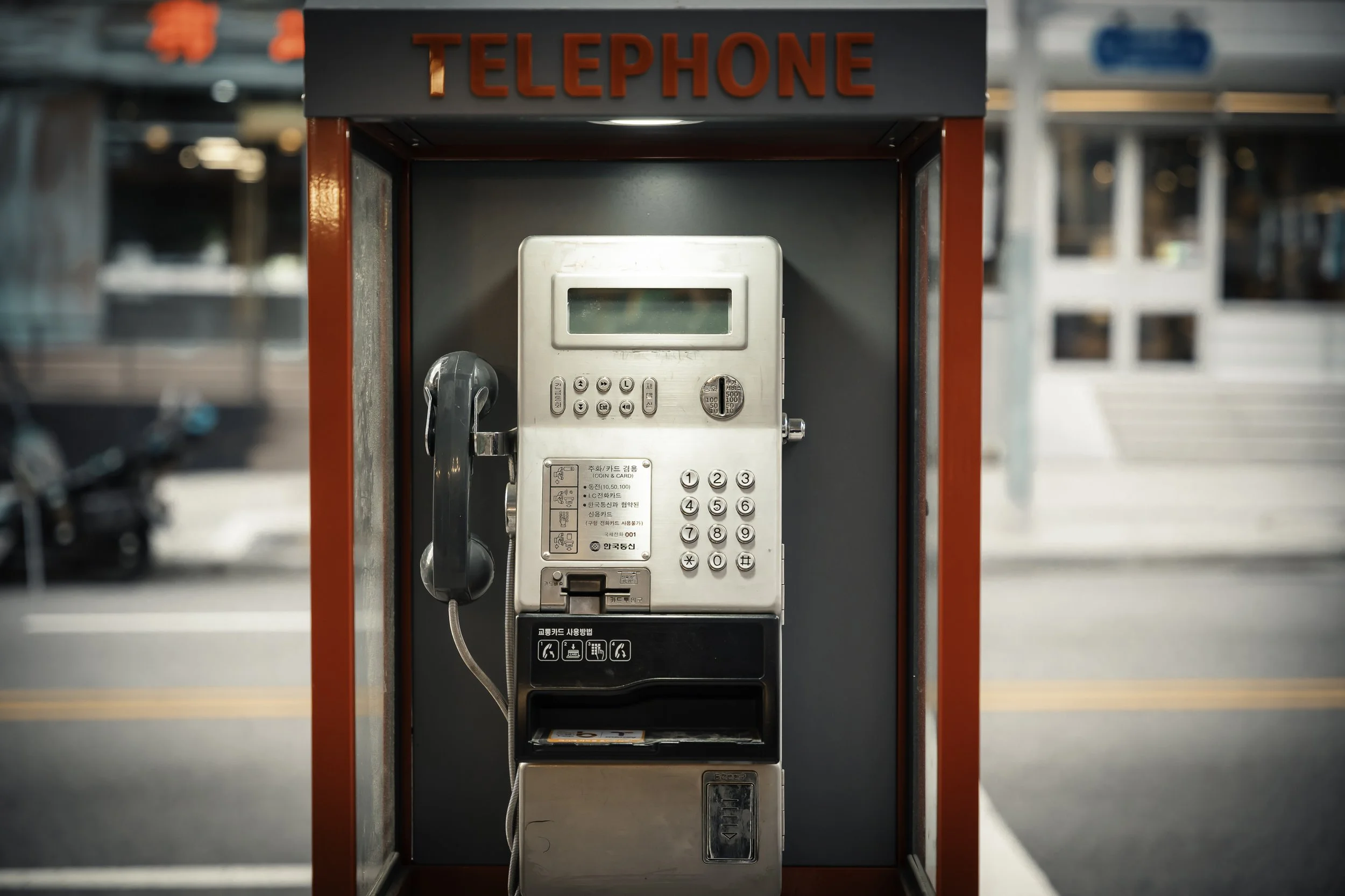 Red outdoor telephone booth with a white payphone inside.