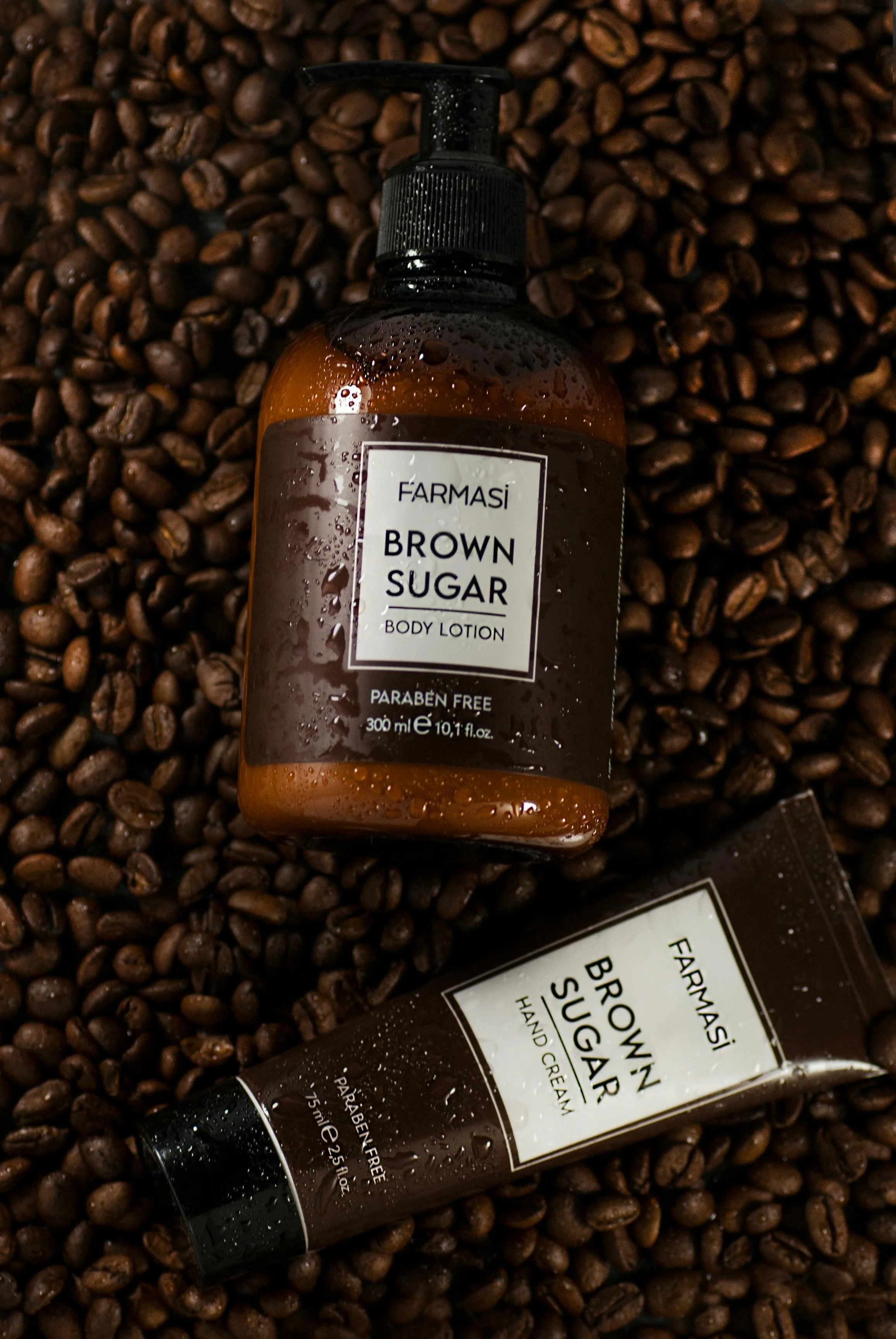A bottle of FarmaSì brown sugar body lotion and a tube of FarmaSì brown sugar hand cream on a bed of coffee beans.