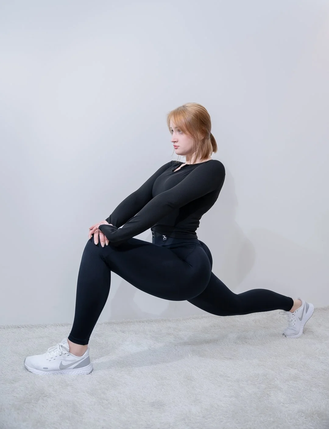 Woman in black athletic wear performing a lunge exercise indoors on a light-colored carpet.