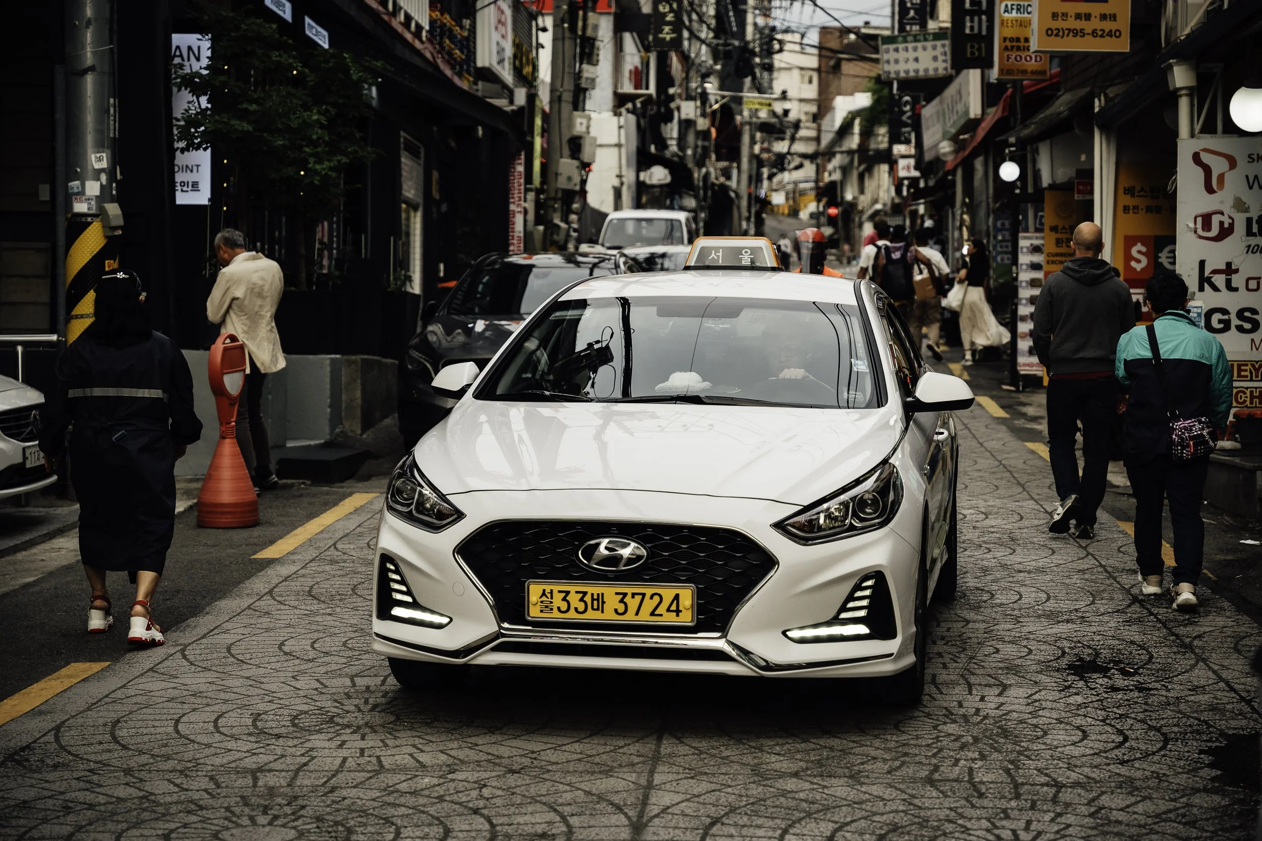 White taxi parked on a busy city street with pedestrians walking on the sidewalk.