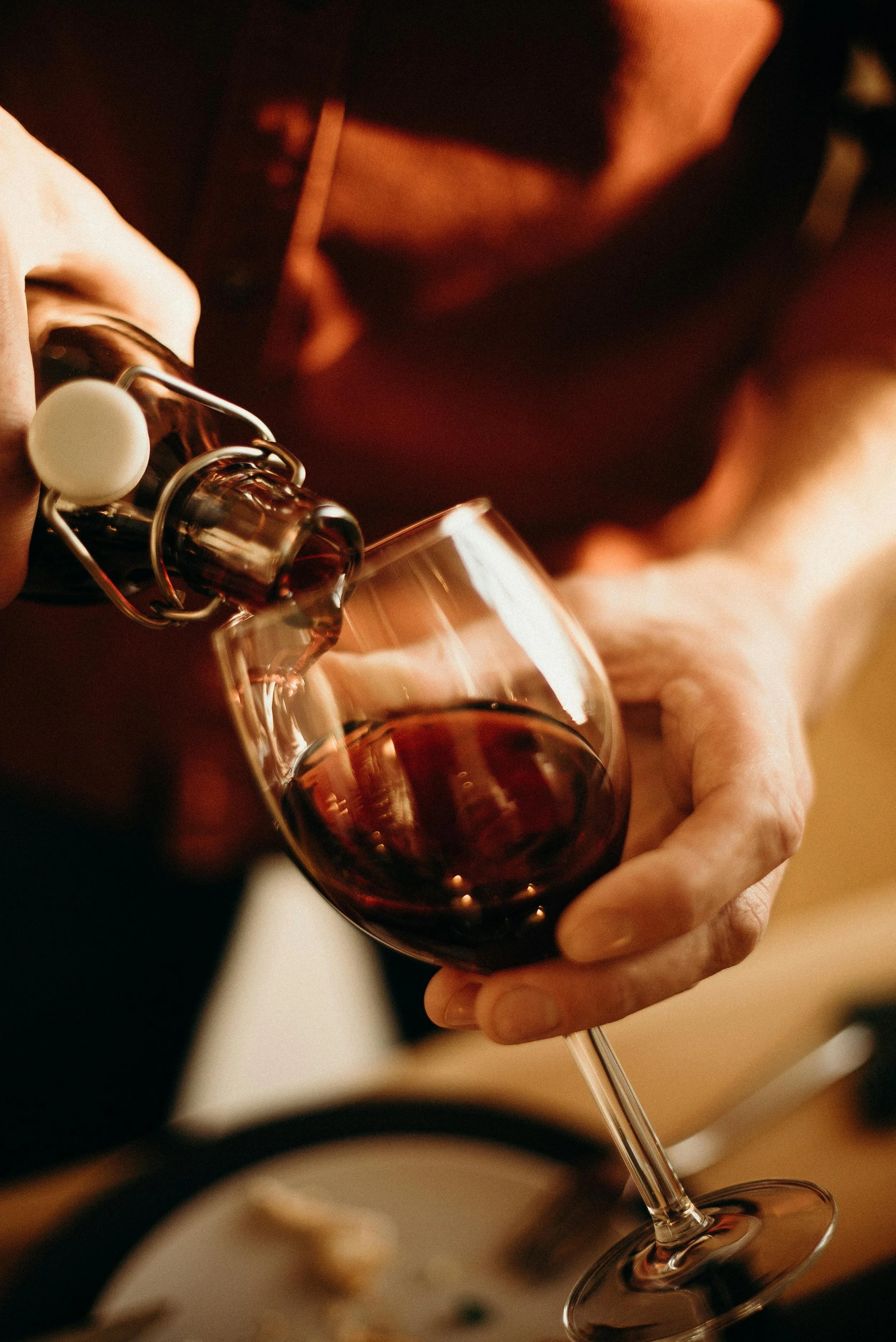 Person pouring red wine into a wine glass from a bottle with a swing-top closure.