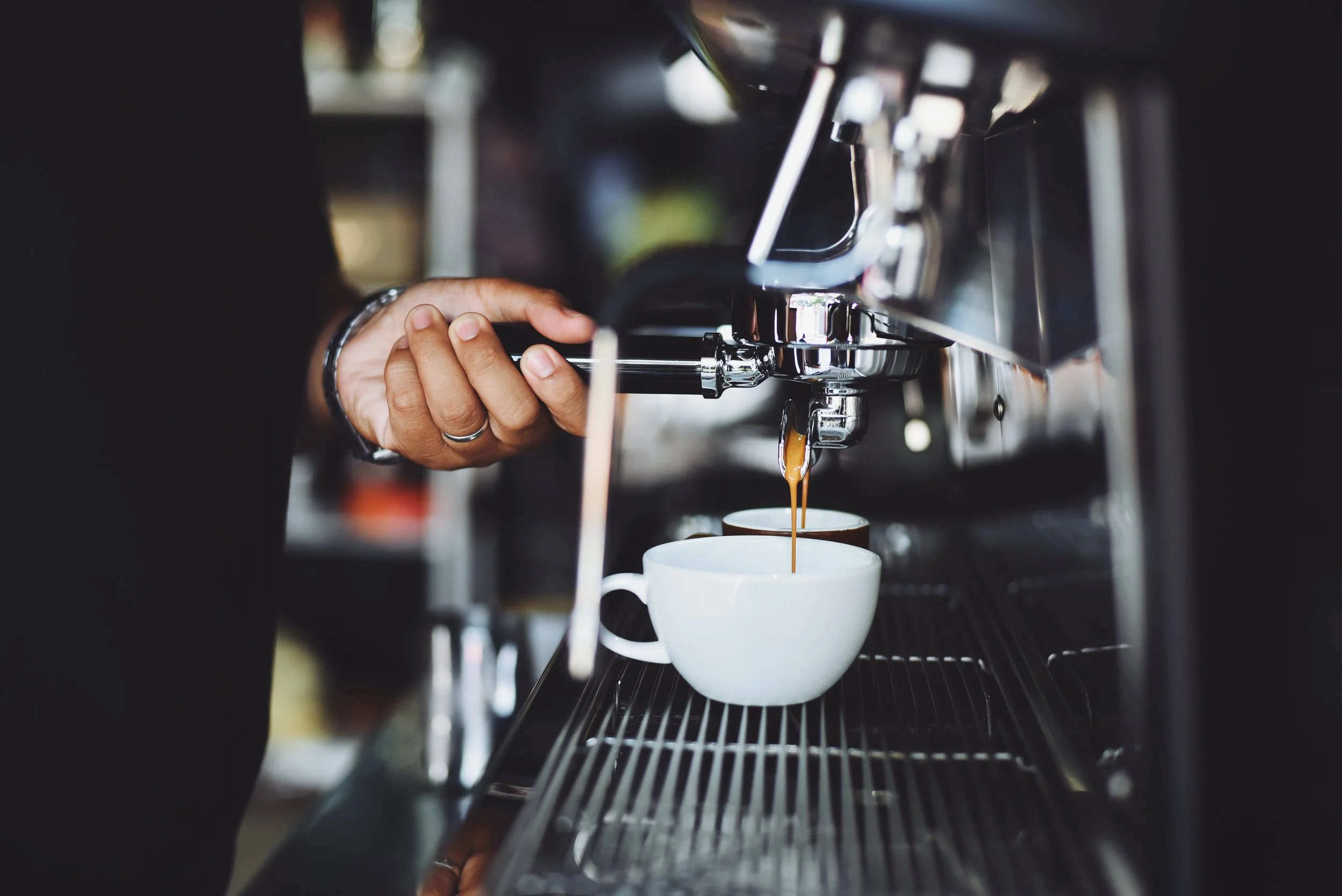 A barista is pulling espresso shot from a coffee machine into white cups.