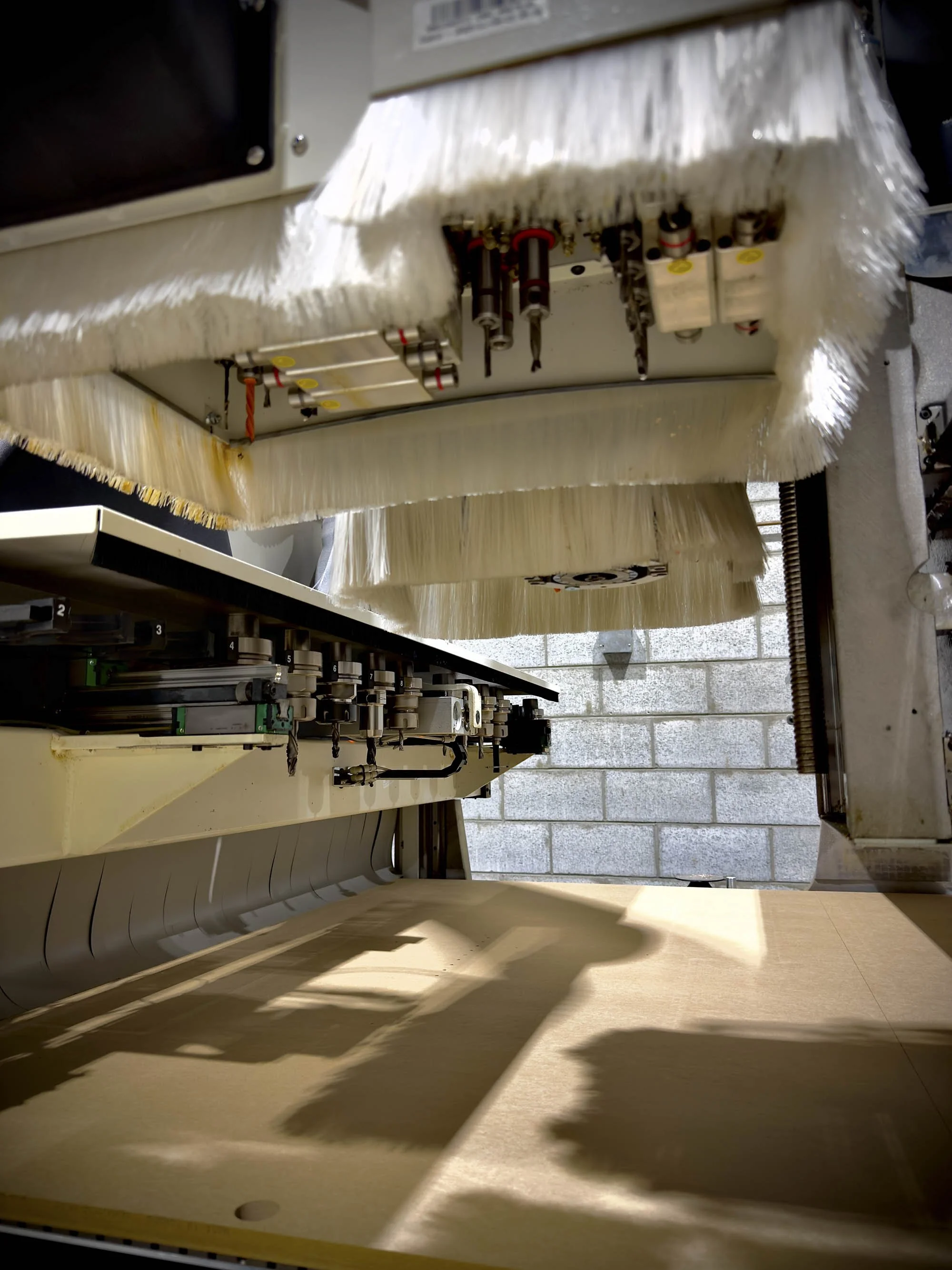 Usinage de panneaux de bois par machine CNC numérique avec têtes de coupe et brosses de protection en action dans notre atelier d'ébénisterie à Boisbriand.