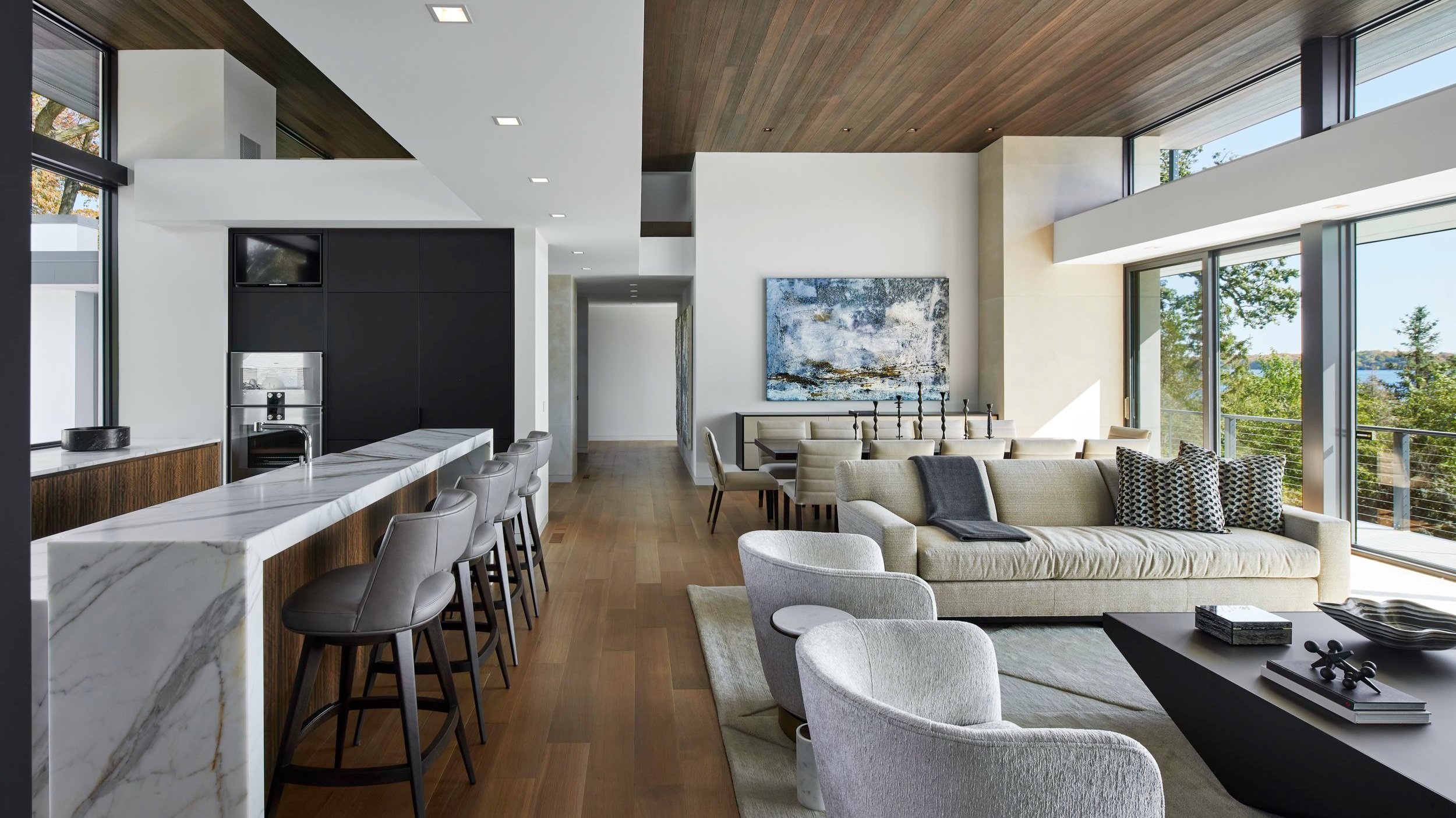 A warm modern open living space that features a living room, dining room, and kitchen. The wood floor and ceiling add warmth to the space.