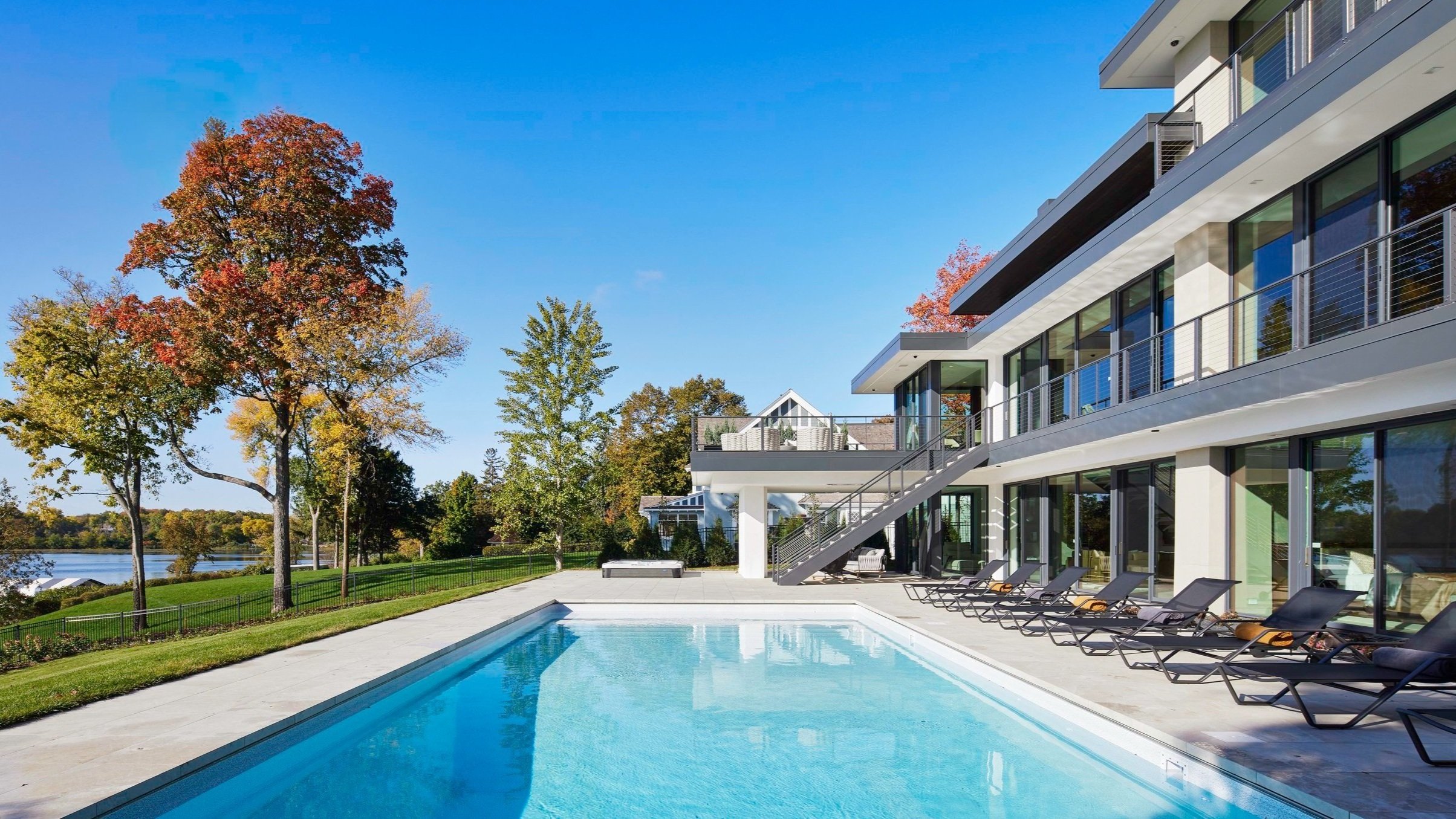 A warm modern lake home with three levels of floor-to-ceiling windows, a pool, and a second-level patio